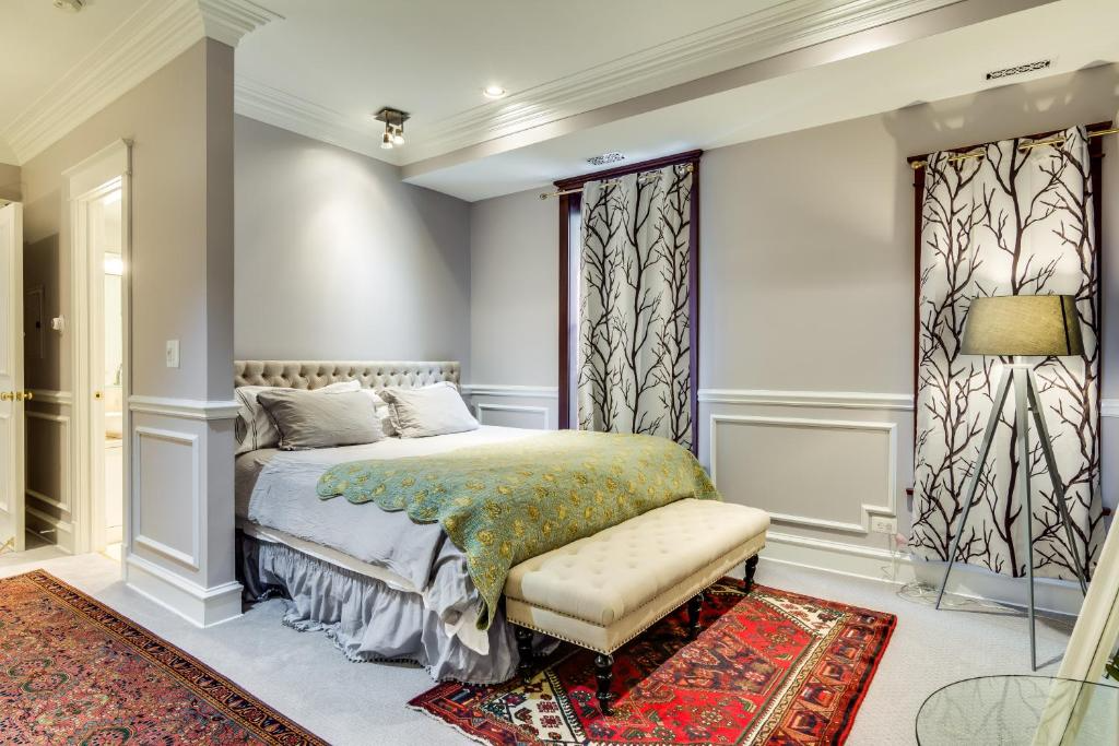 Bedroom with bed, bench, patterned rug, curtains, and lamp. Gray walls, white trim.