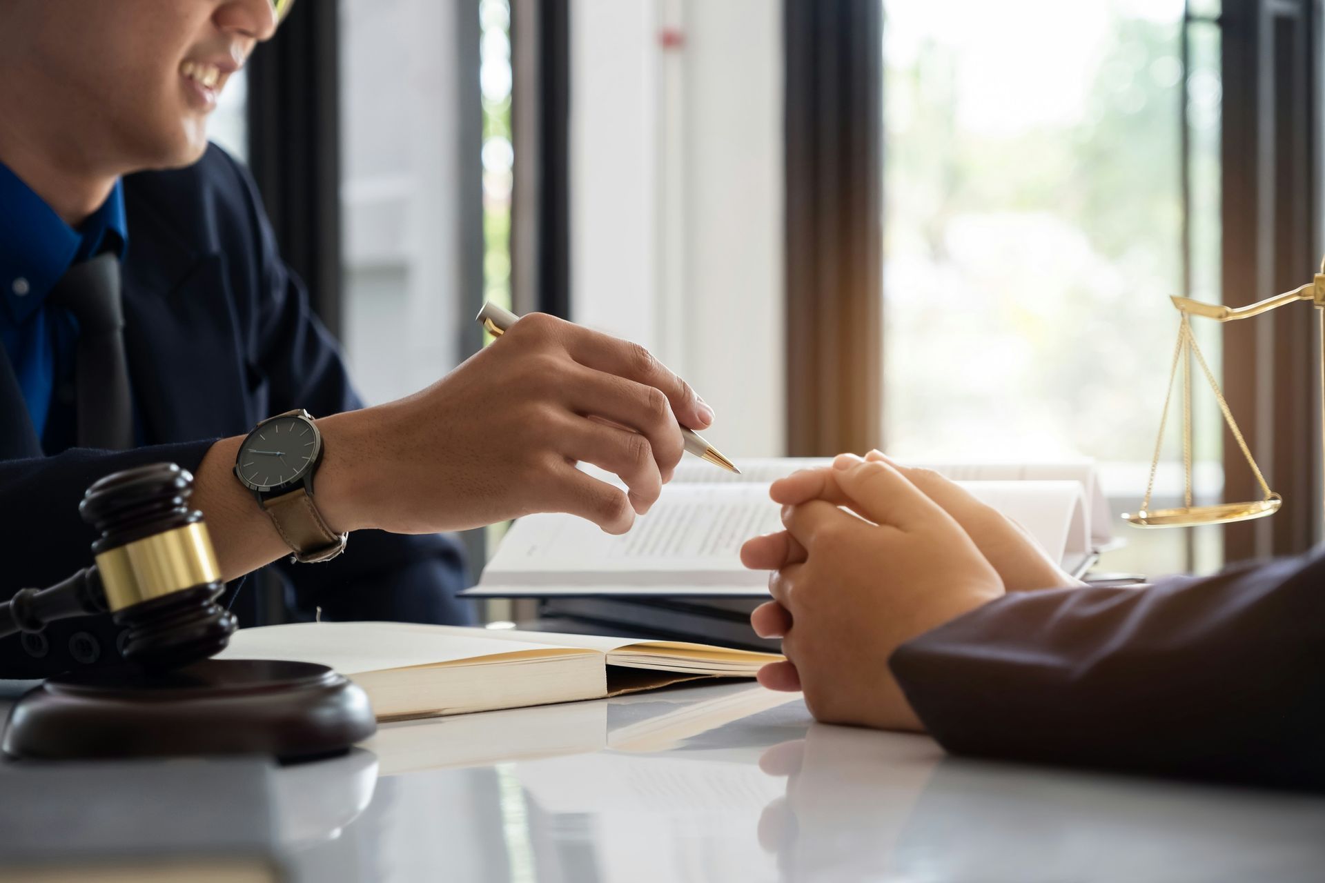 Two people discuss a contract at a desk, with a gavel and scales of justice nearby.