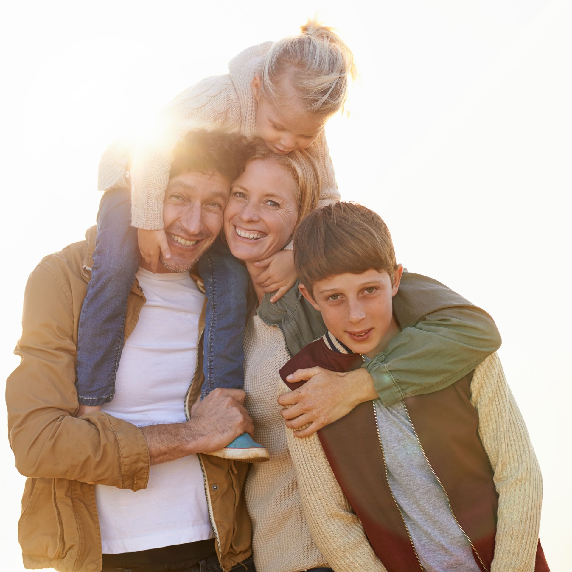Smiling family of four hugging outdoors in bright sunlight