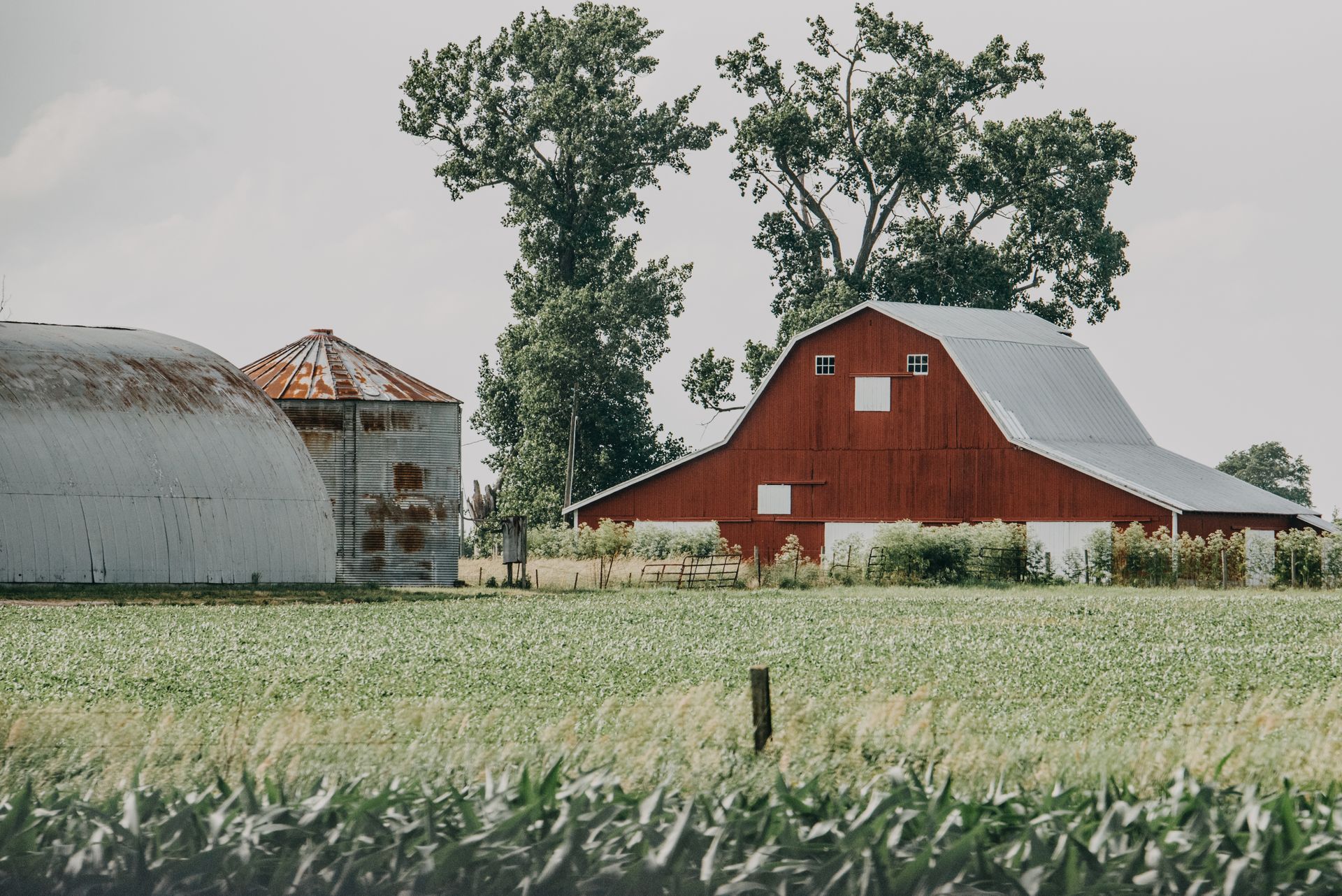 Red barn and silos in a grassy rural field under cloudy sky