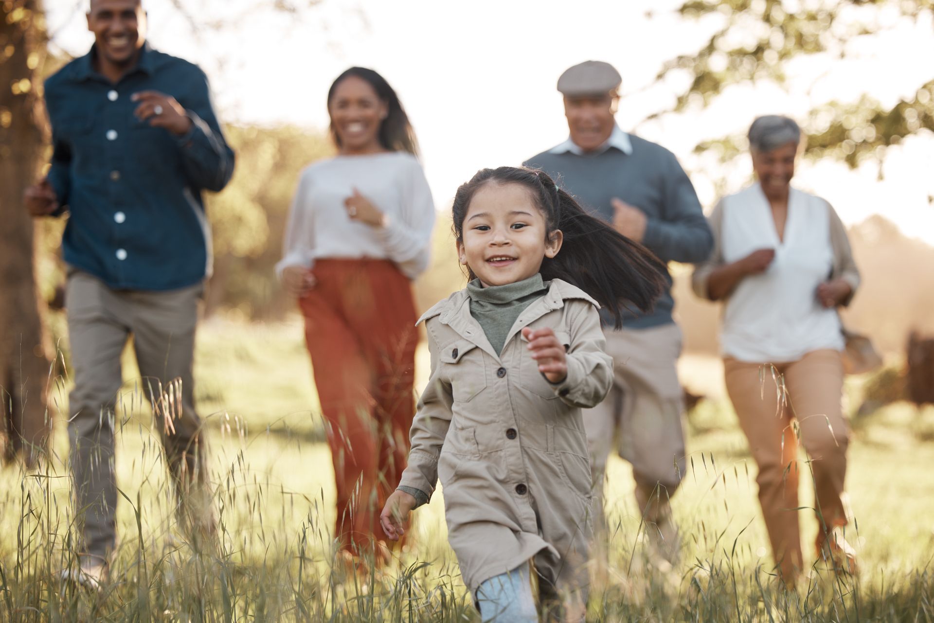 Family running together through a sunlit grassy field outdoors, with a smiling child in front