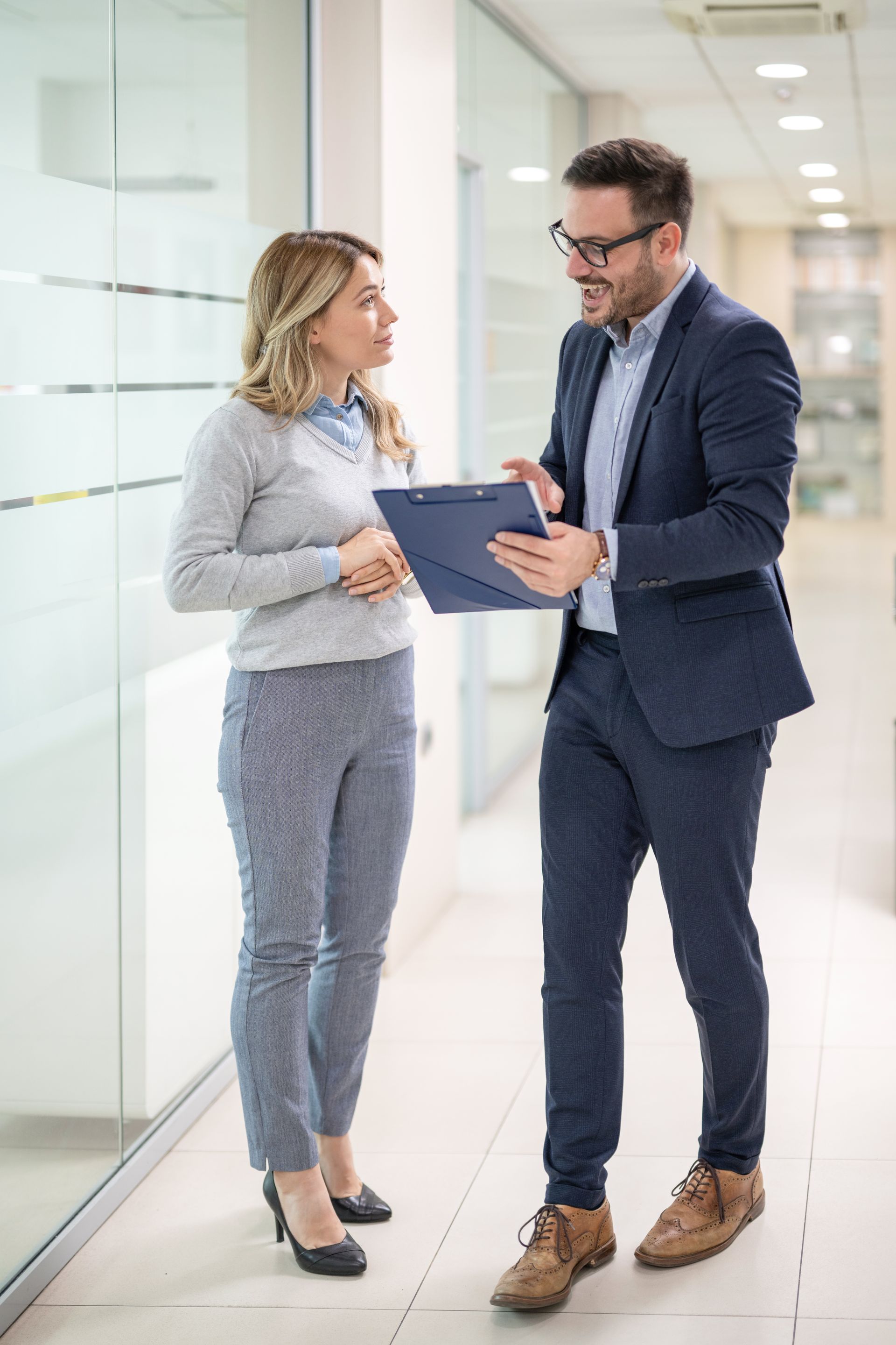 Two professionals reviewing a tablet in a bright office hallway