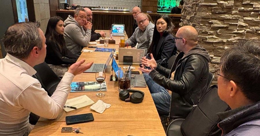 A group of people are sitting around a table with laptops.