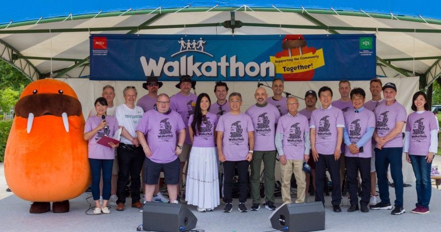Group of volunteers in purple shirts standing on stage beside the mascot at the 35th Walkathon