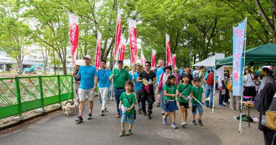 NIS students walking through a tree-lined park path with red flags and a green fence on the left