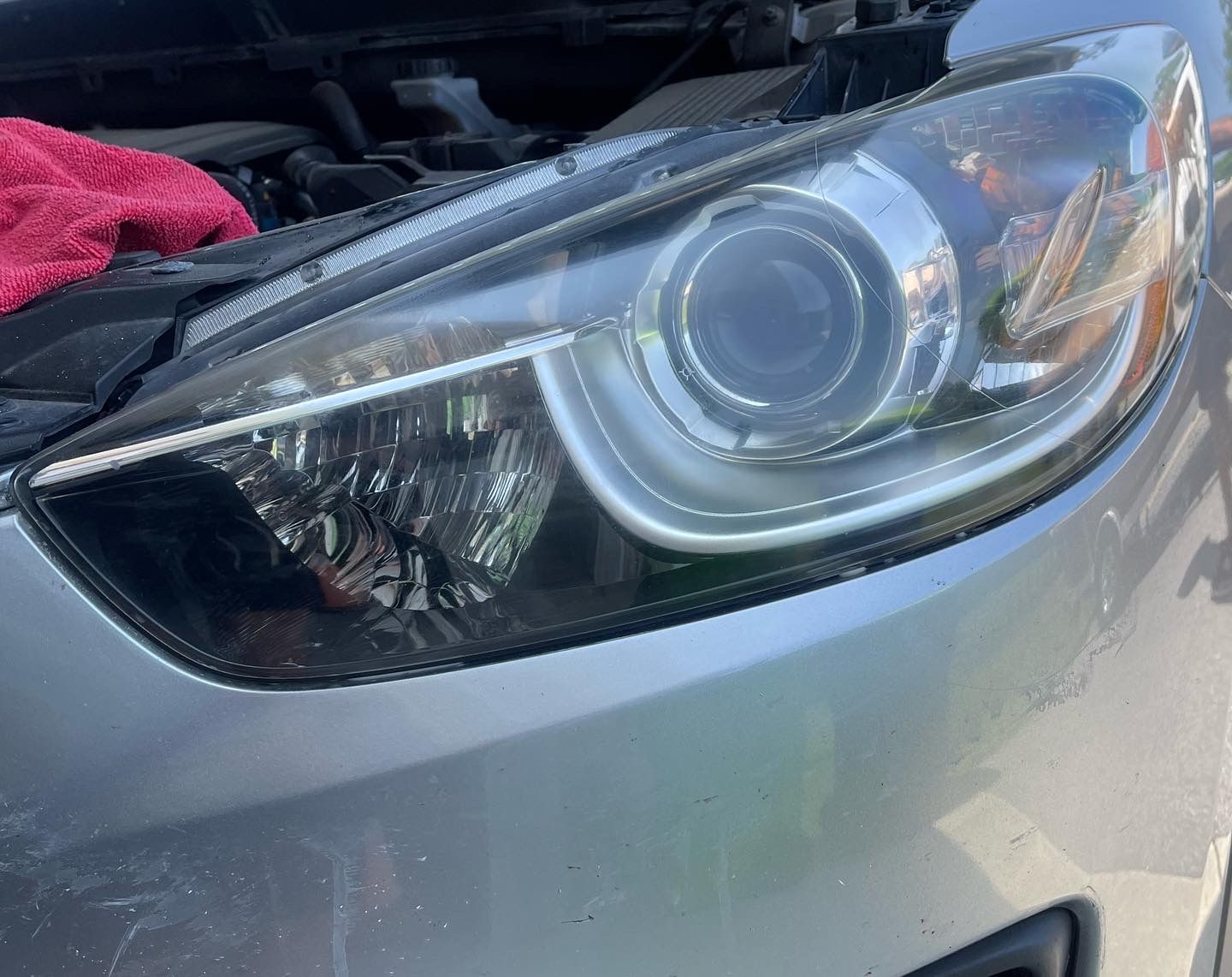A close up of a car headlight with the hood open.