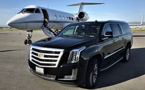 Black Cadillac SUV parked in front of a private jet on a tarmac.