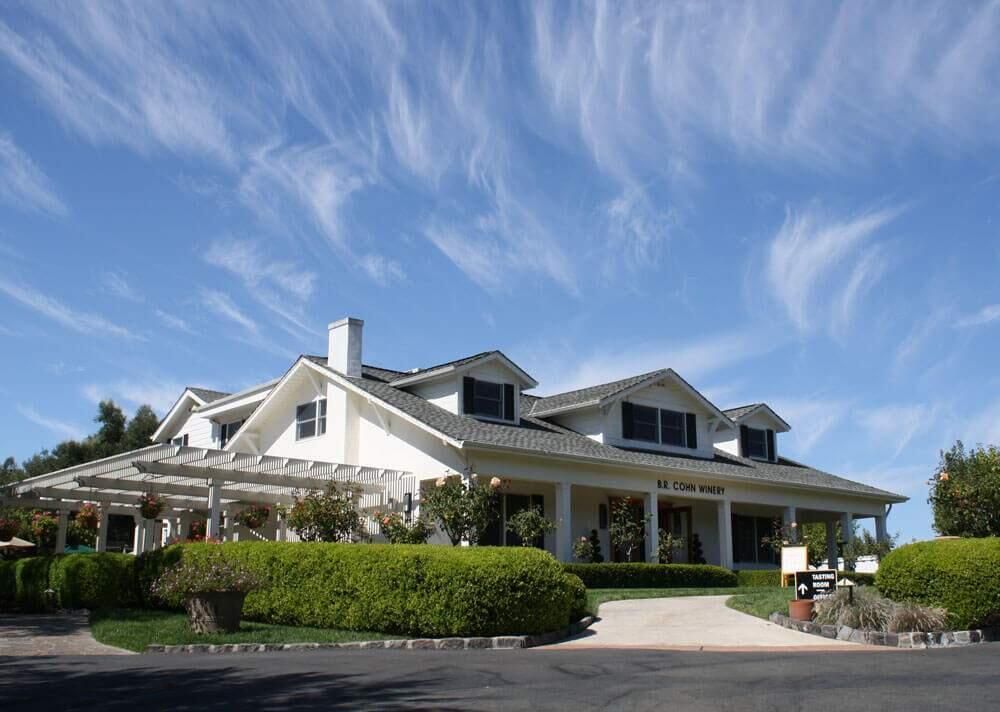 White building with dark roof, arbor, and landscaping against a blue sky with wispy clouds.