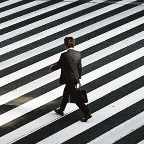 Man in suit walking across a diagonal zebra crossing, carrying a briefcase.