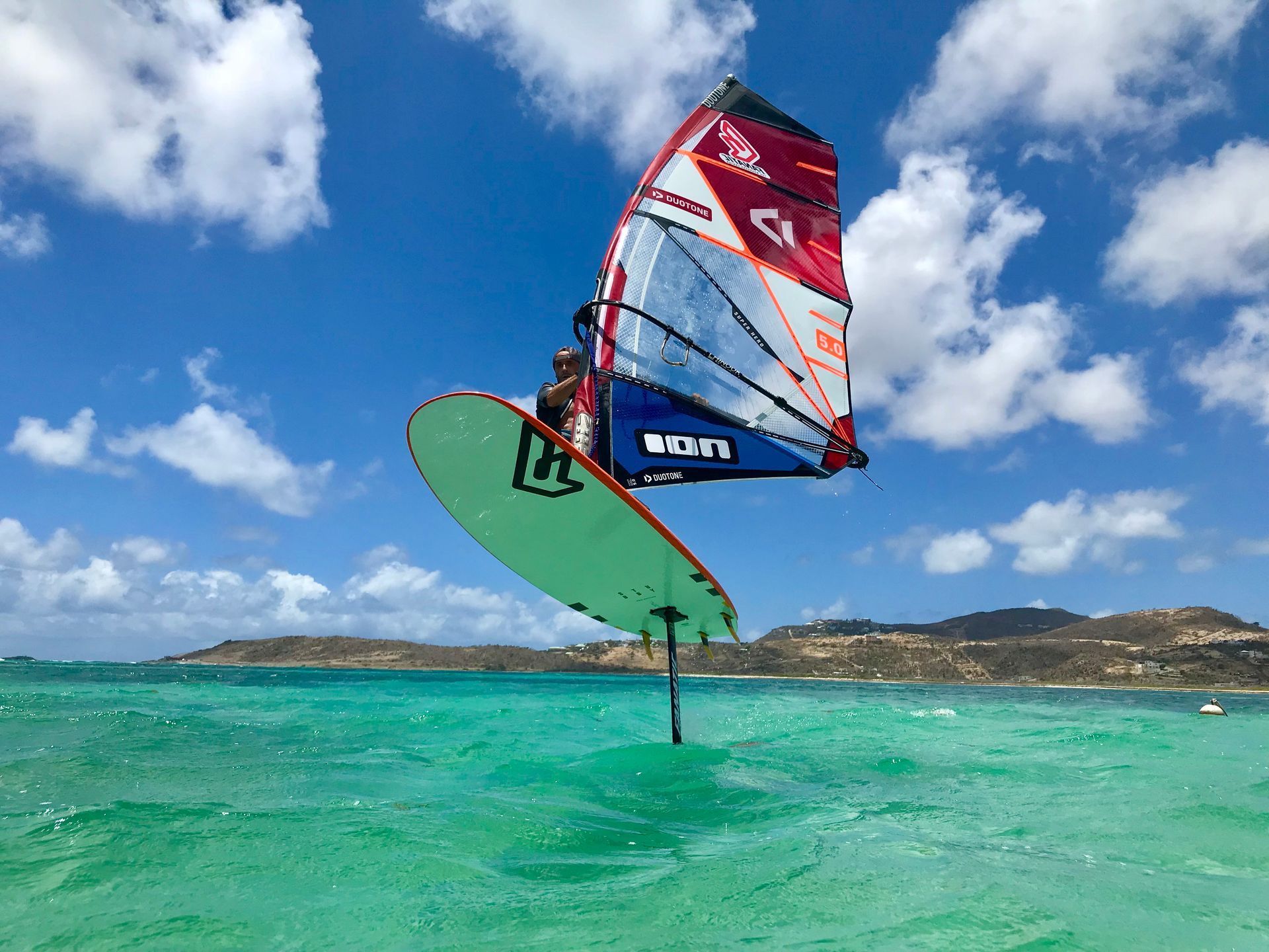 A person is flying through the air while riding a surfboard in the ocean. Wingfoil