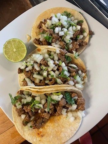 A white plate topped with three tacos and a lime slice.