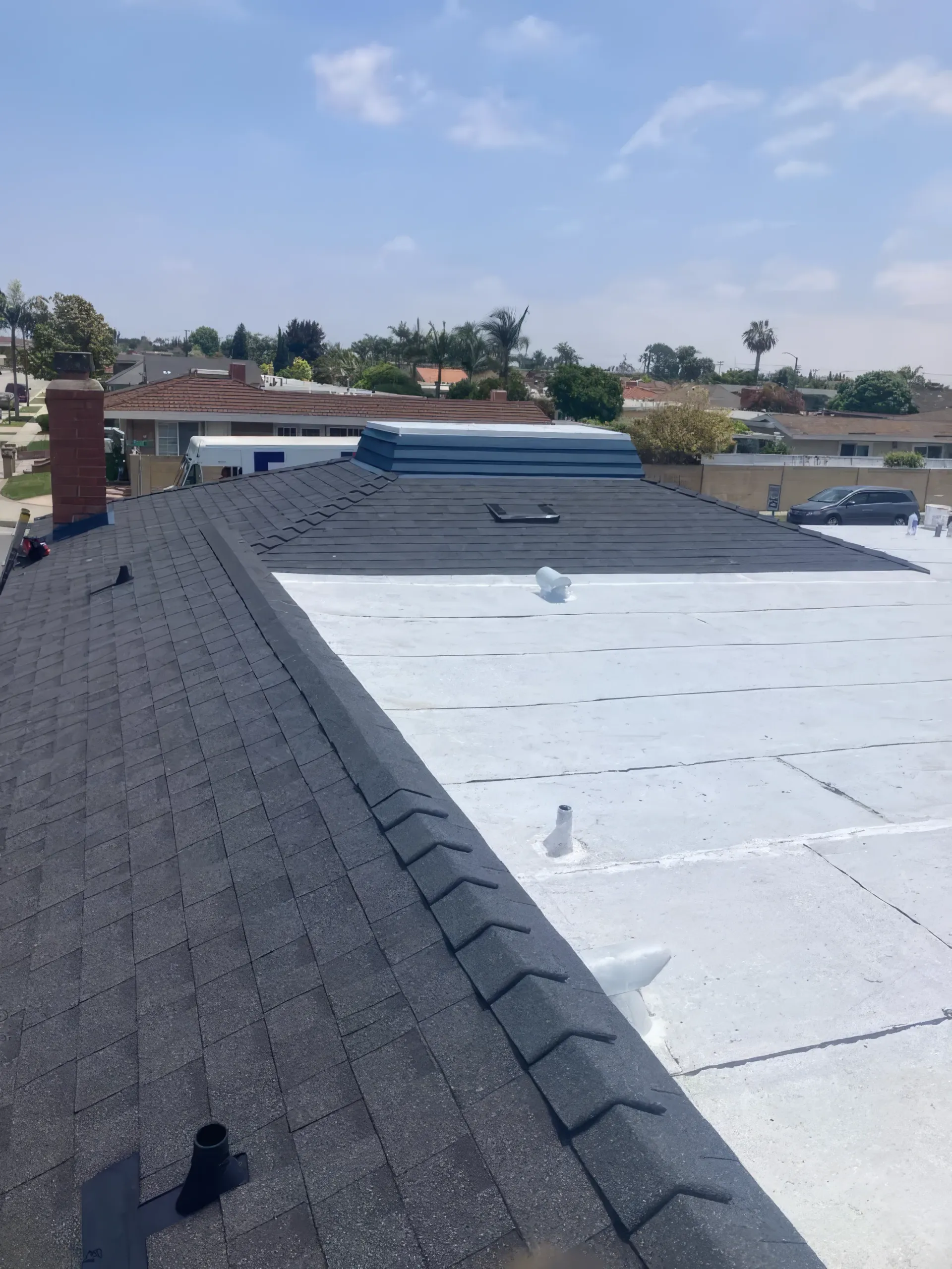 Rooftop with dark shingle sections and a white flat roof under a partly cloudy sky.