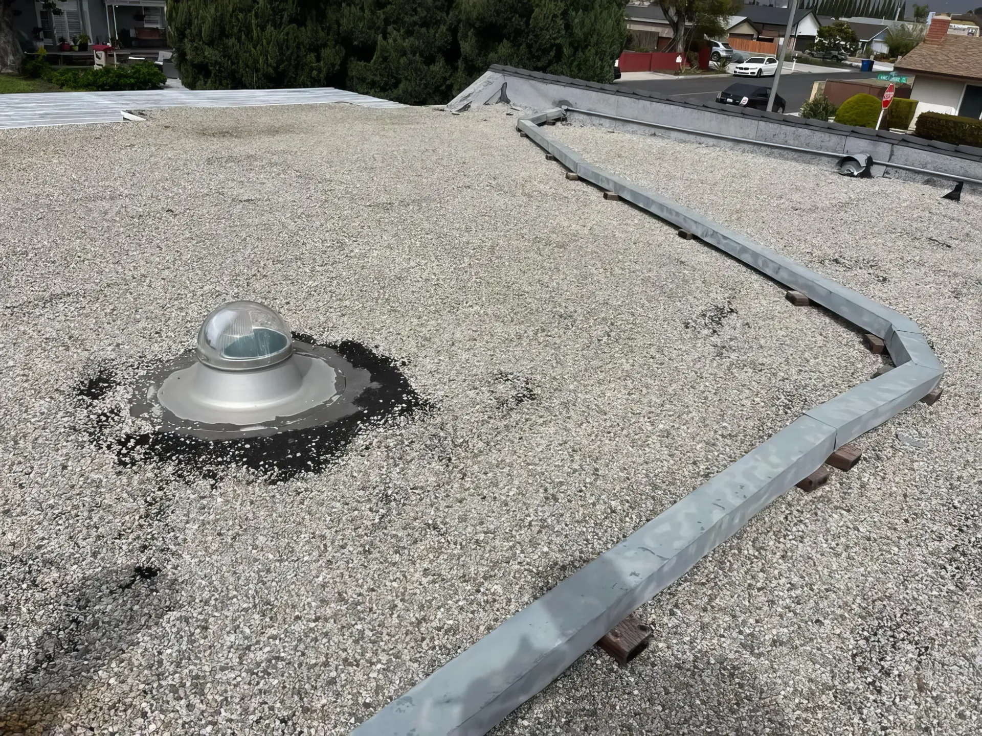 Gravel rooftop with a round skylight and a gray metal flashing border around the edge