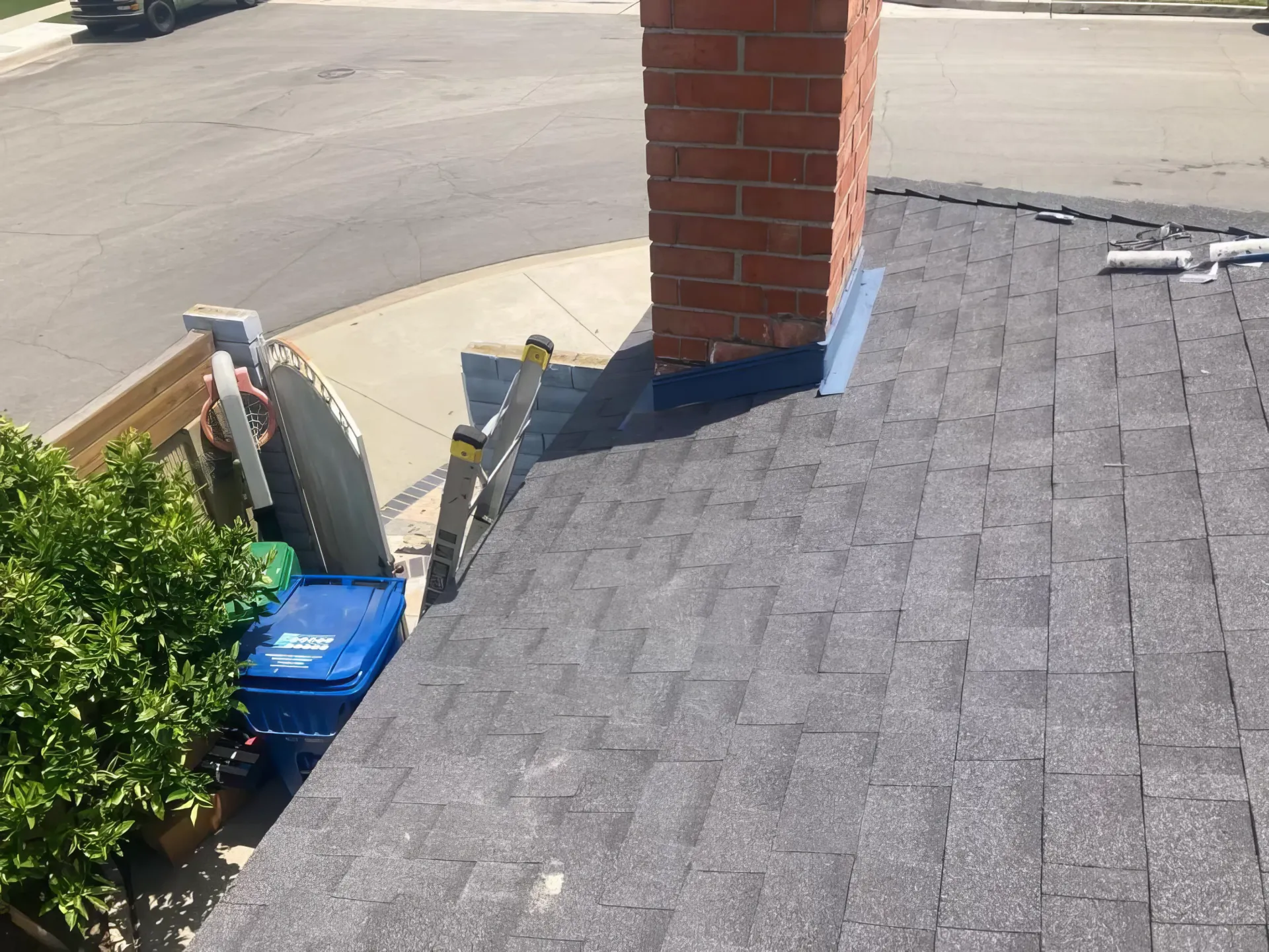 Rooftop near brick chimney, with ladder, blue box, and street below visible at the edge
