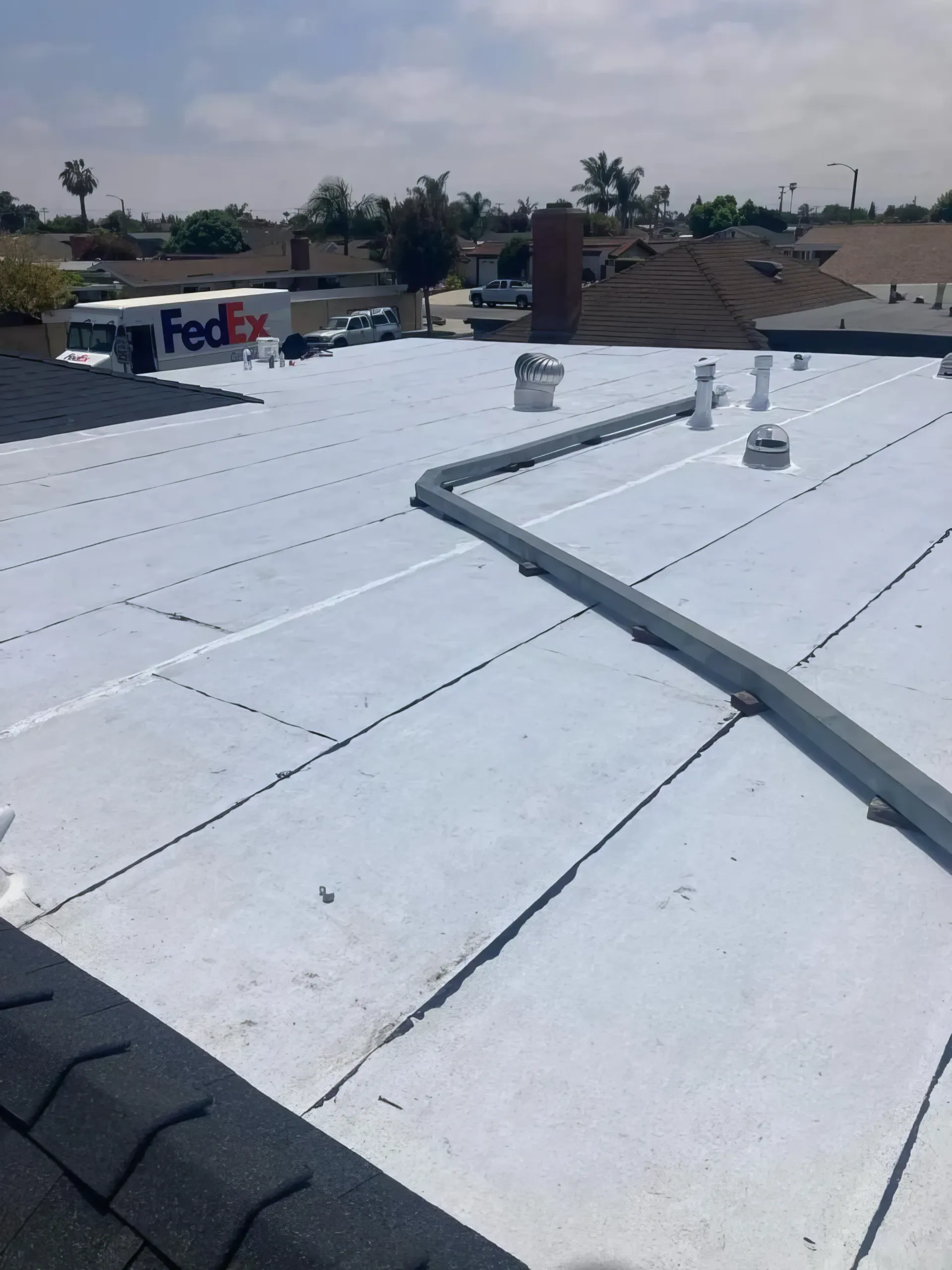 White commercial rooftop with HVAC vents and ducts under a cloudy sky, buildings in the distance