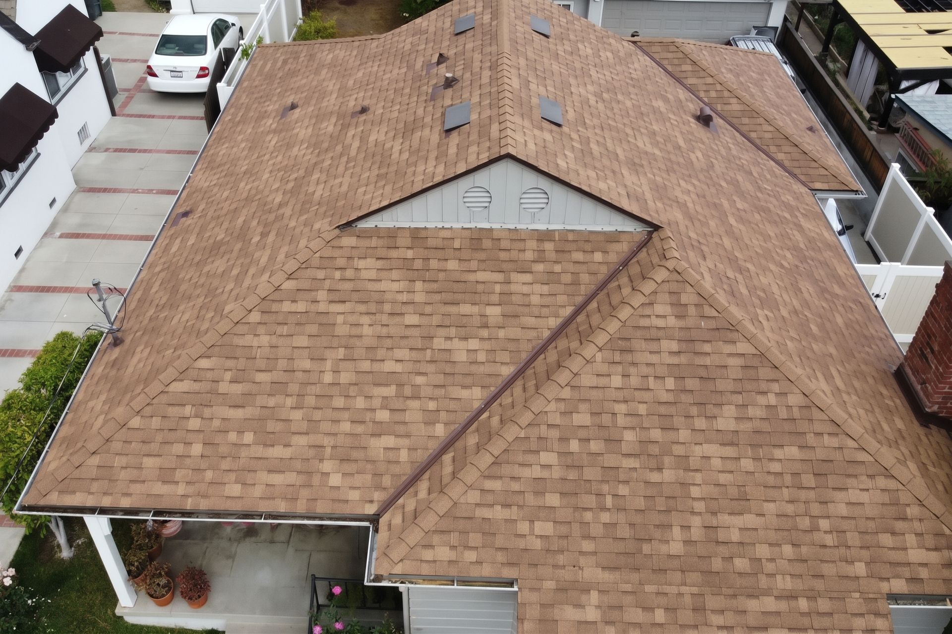 Aerial view of a tan shingle roof on a suburban house with a small dormer window.