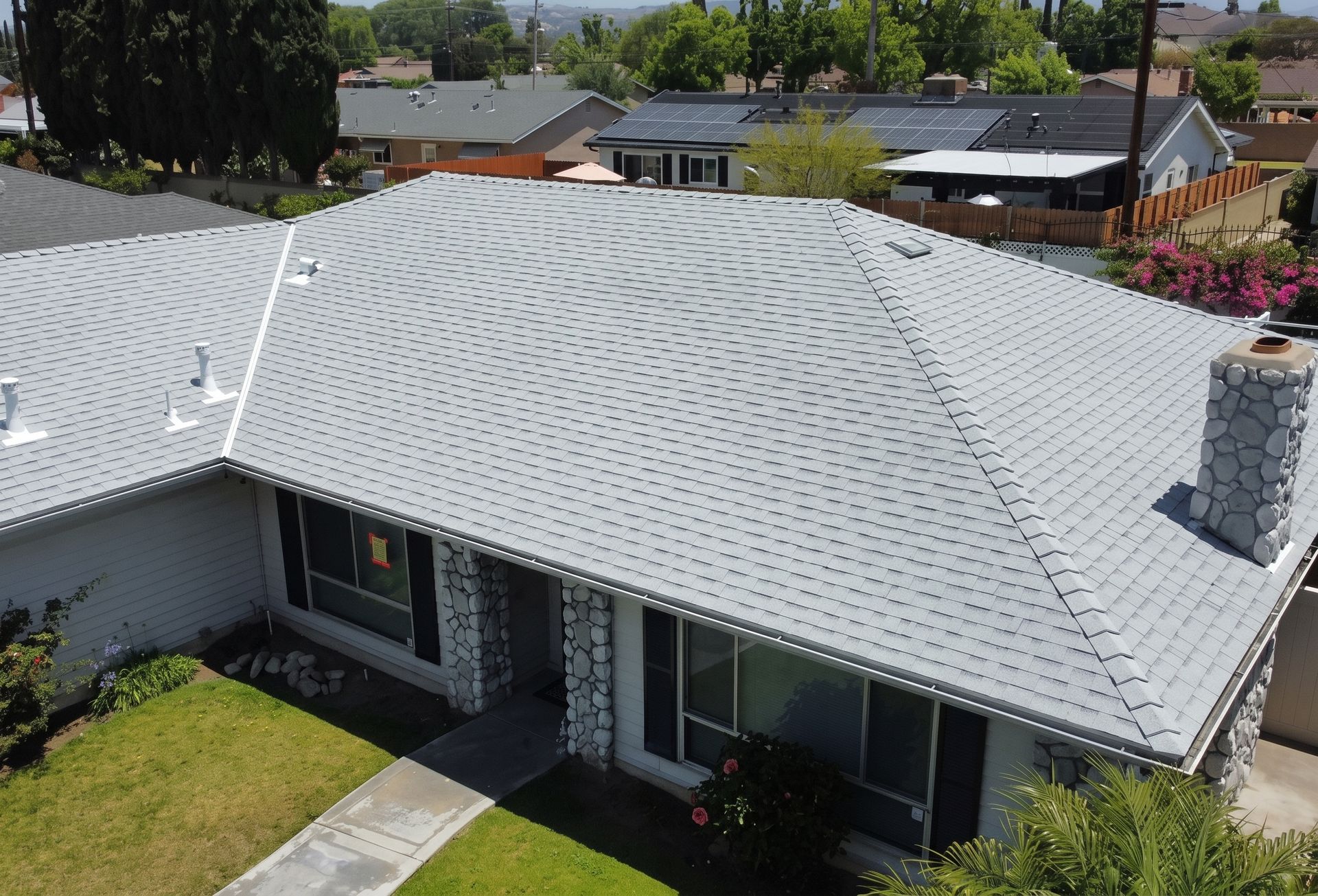 Aerial view of a house with a gray shingle roof and small front yard in a suburban neighborhood