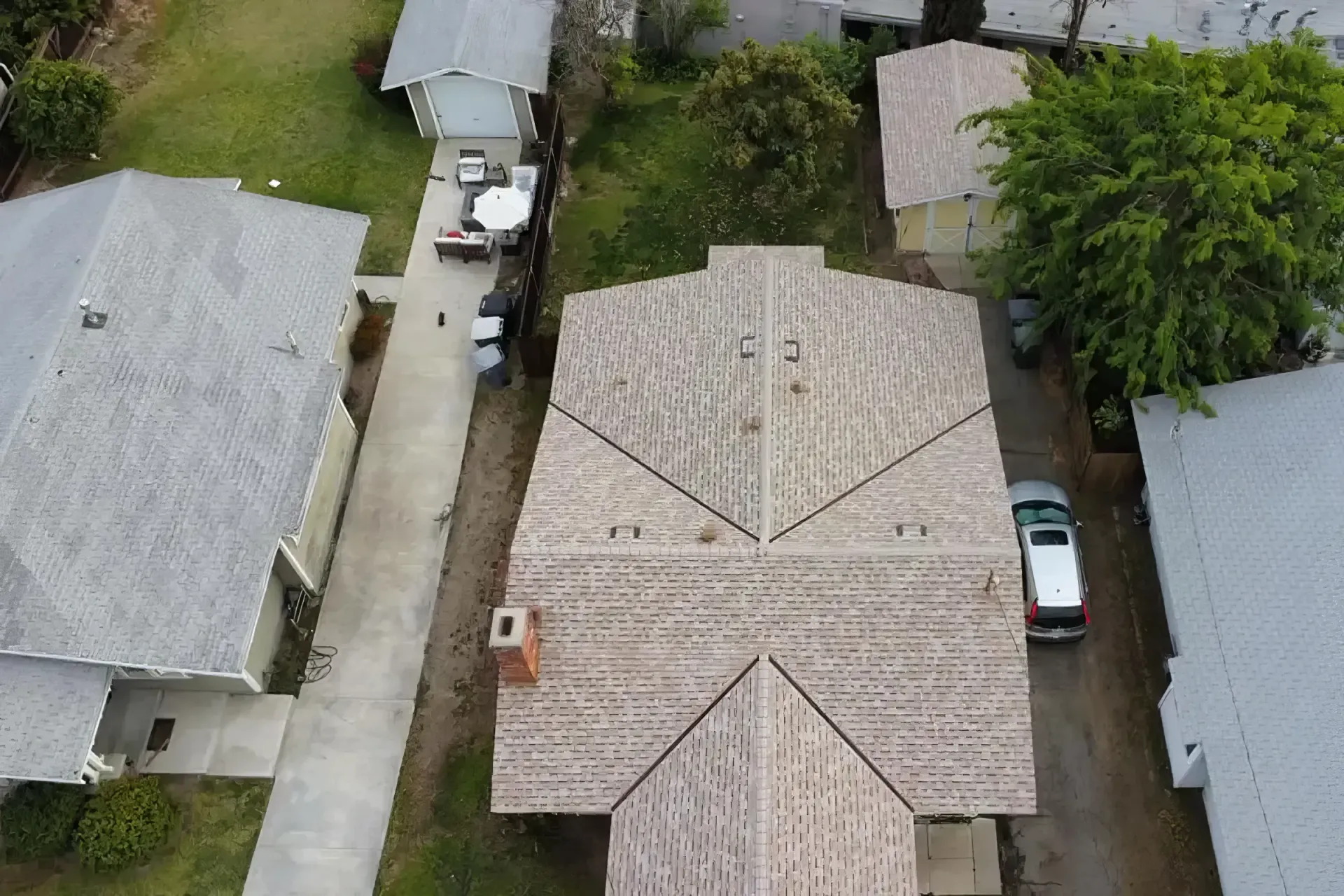 Aerial view of a residential neighborhood with several houses, driveways, trees, and parked cars.