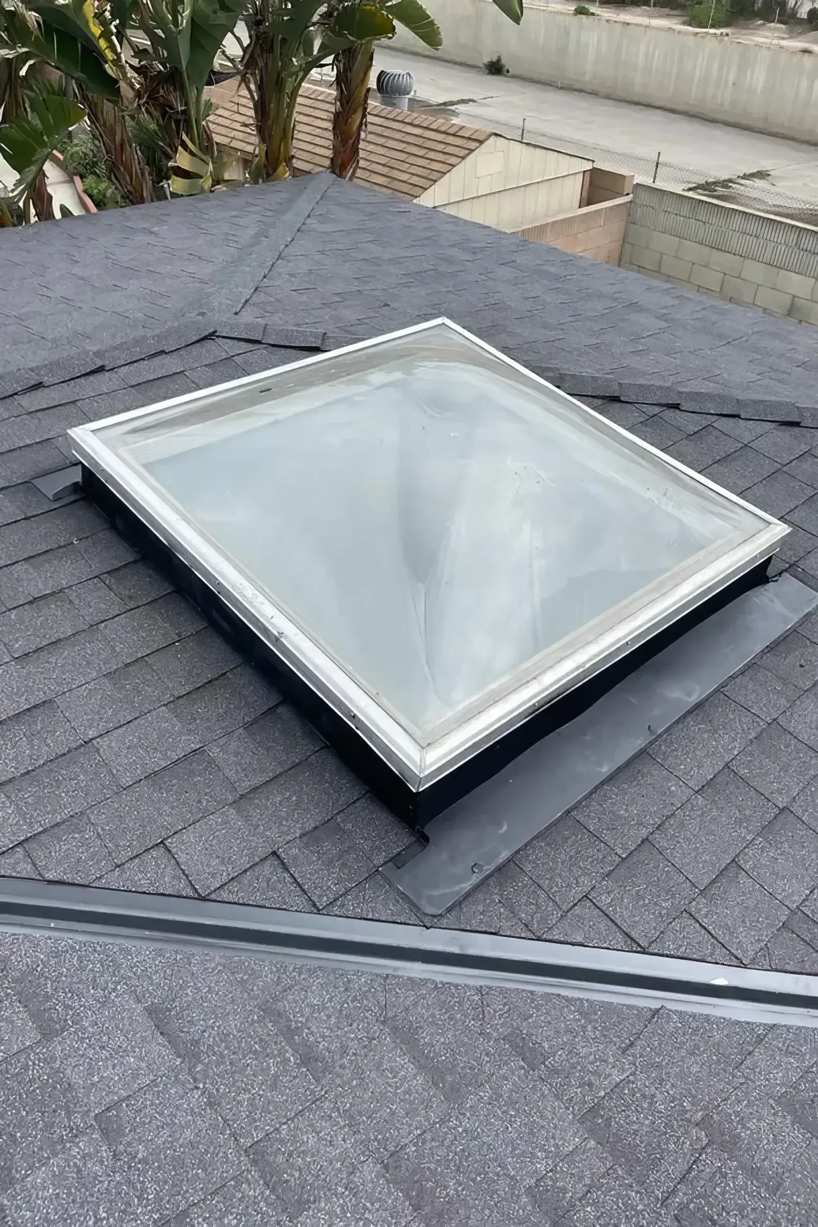 Rooftop skylight with a white frame set into gray asphalt shingles.
