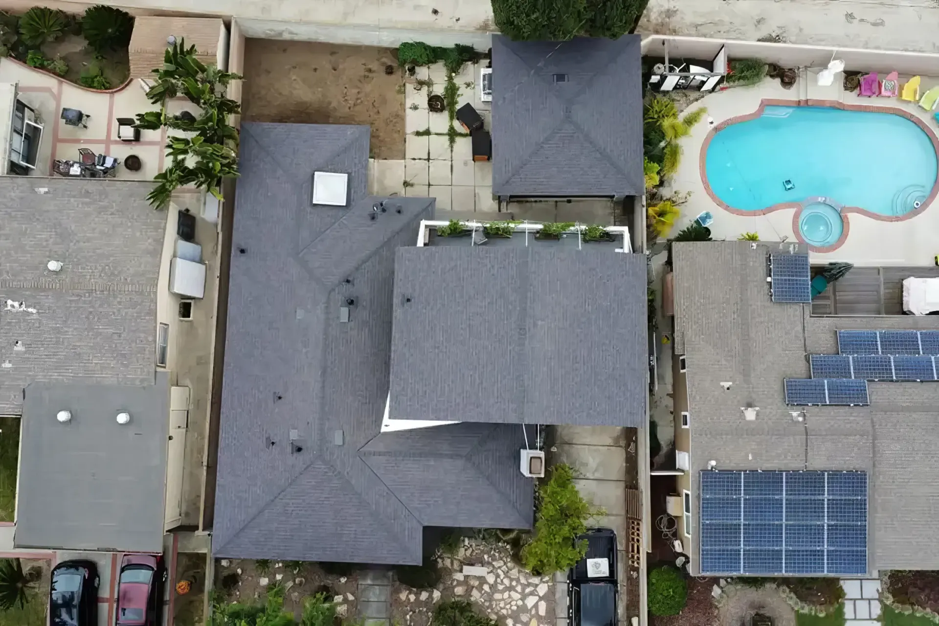 Aerial view of a house with a backyard pool and solar panels, surrounded by paved walkways and greenery