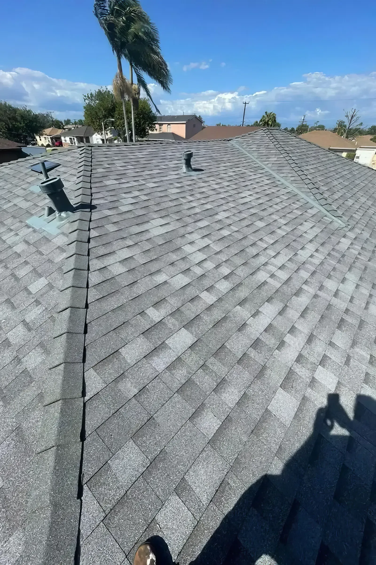 Gray shingled roof with rooftop vent under a blue sky, viewed from above
