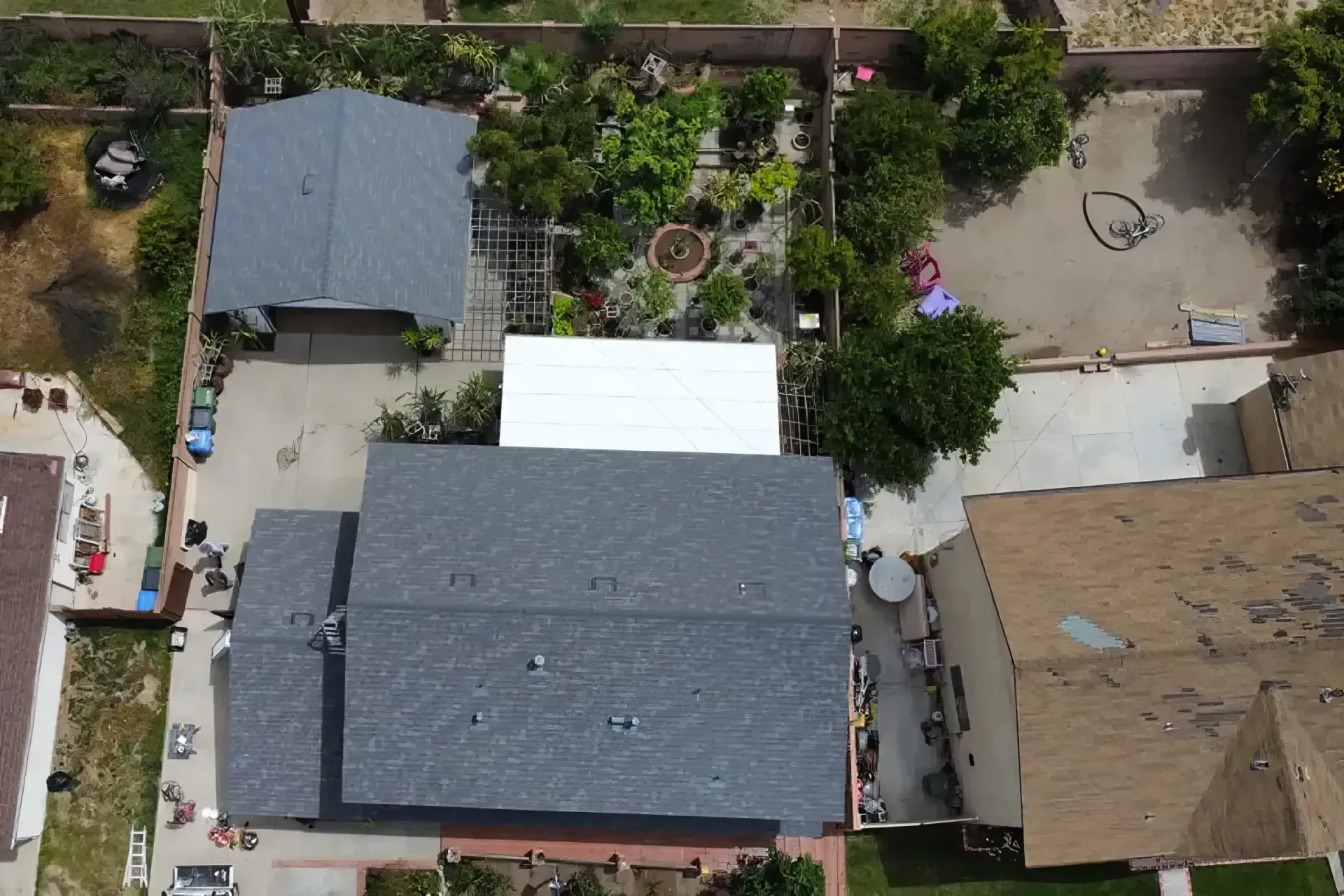 Aerial view of a residential compound with several rooftops, courtyard, trees, and surrounding walls.