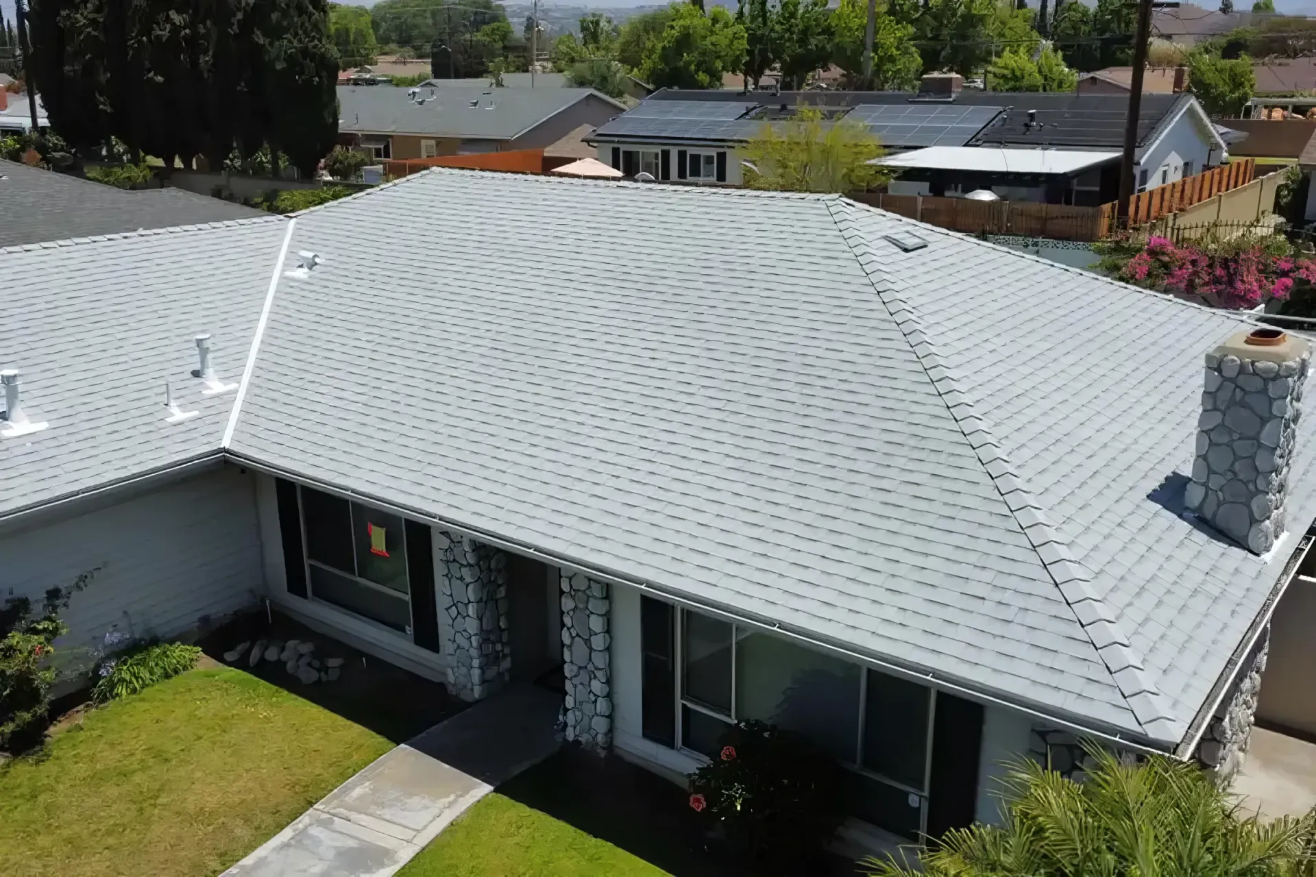 Aerial view of a white-roofed house with a front yard and chimney in a suburban neighborhood