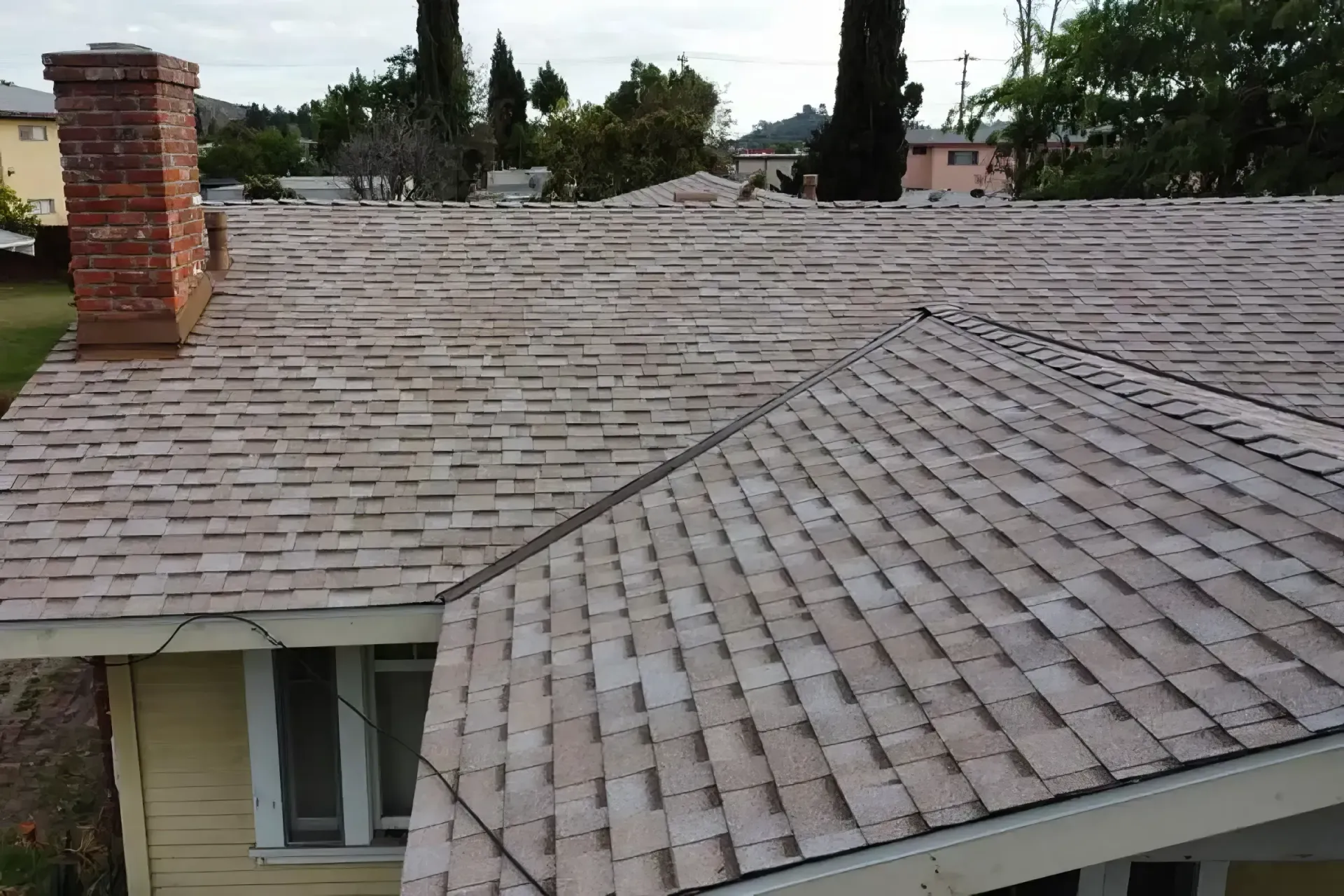 Rooftop with gray shingles and a brick chimney, viewed from above.