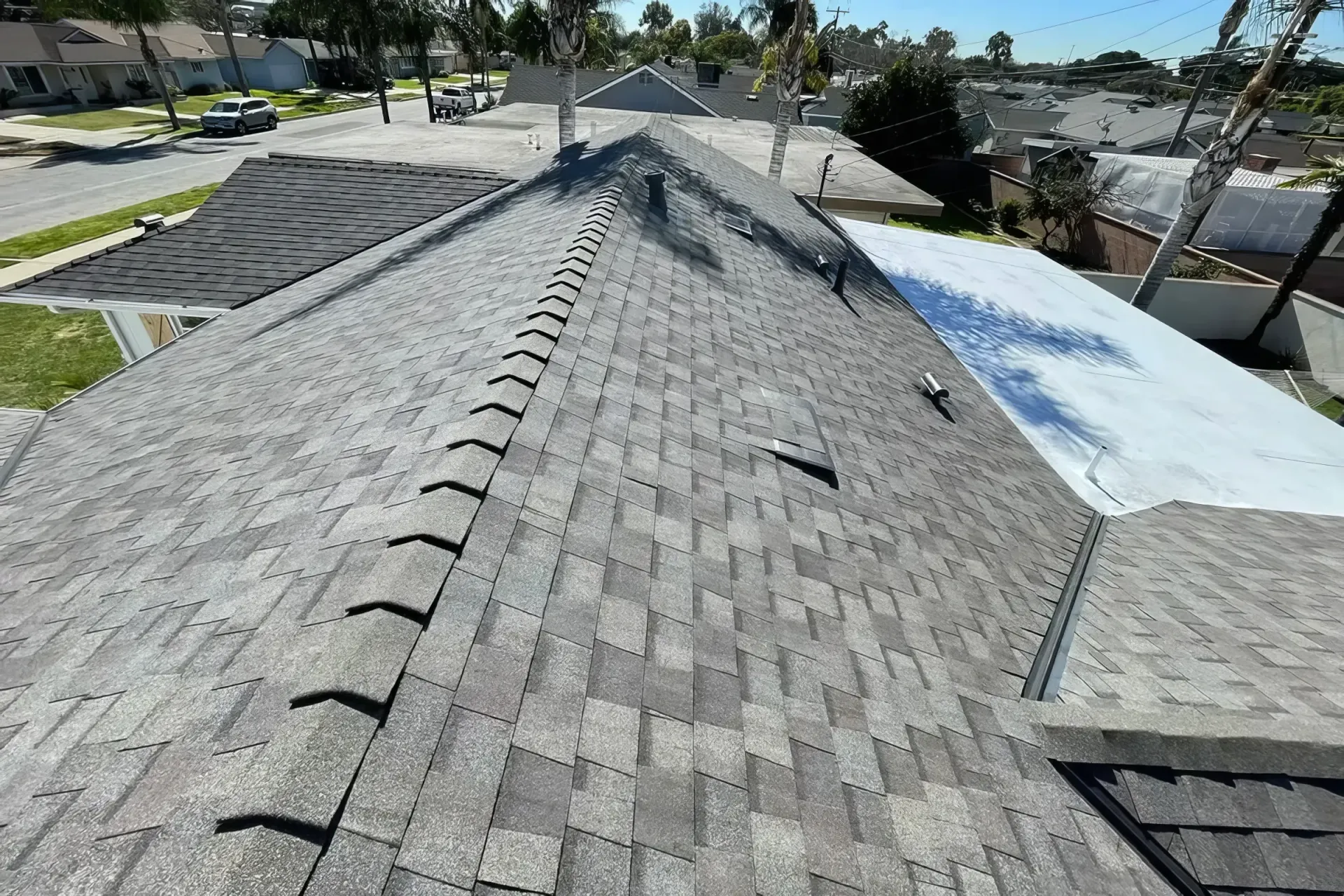 Roof shingles with a central ridge, showing weathered gray and a blue tarp on the right side.