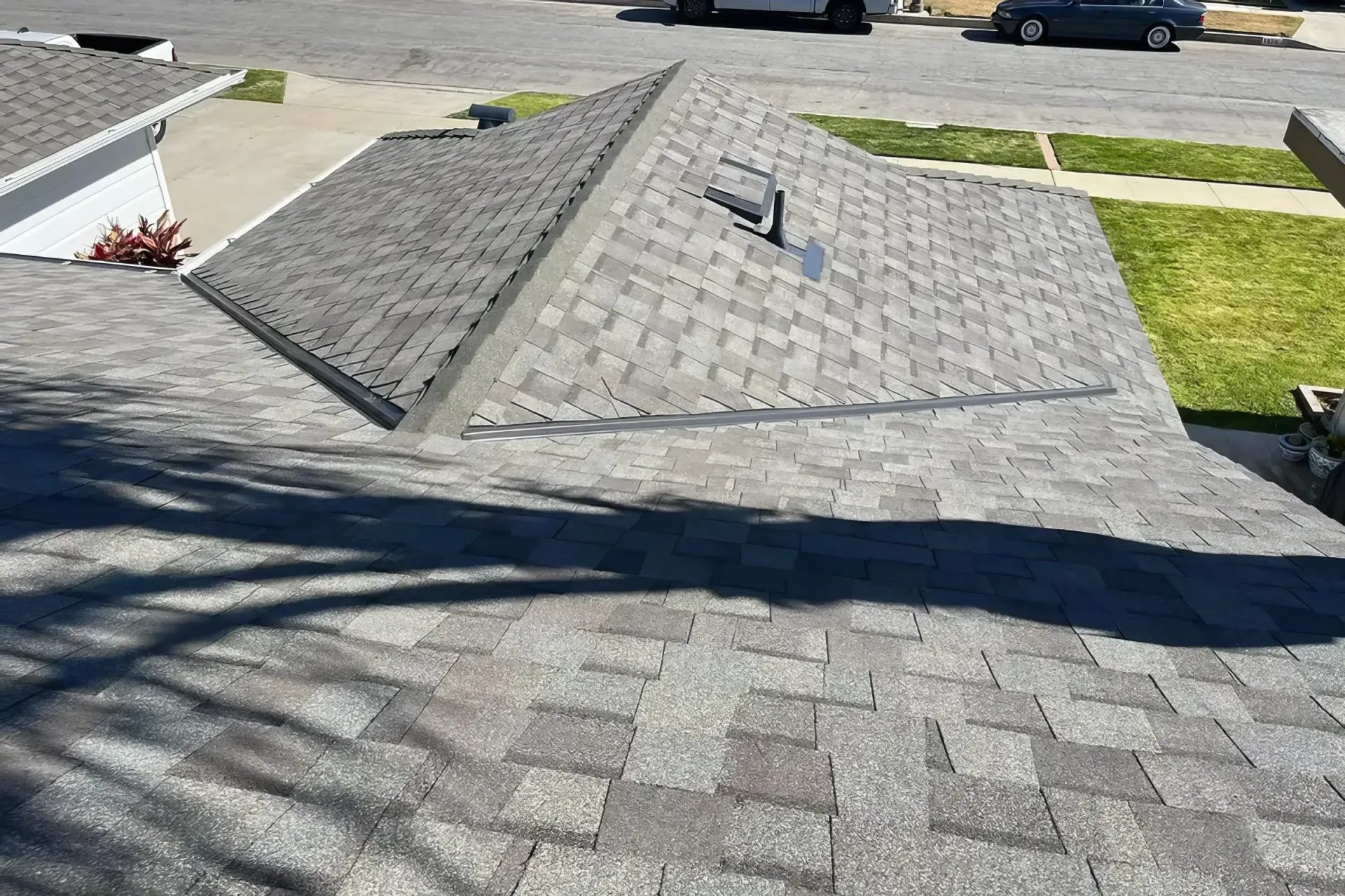 Gray shingled roof with a metal vent pipe and a dark tree shadow across the surface