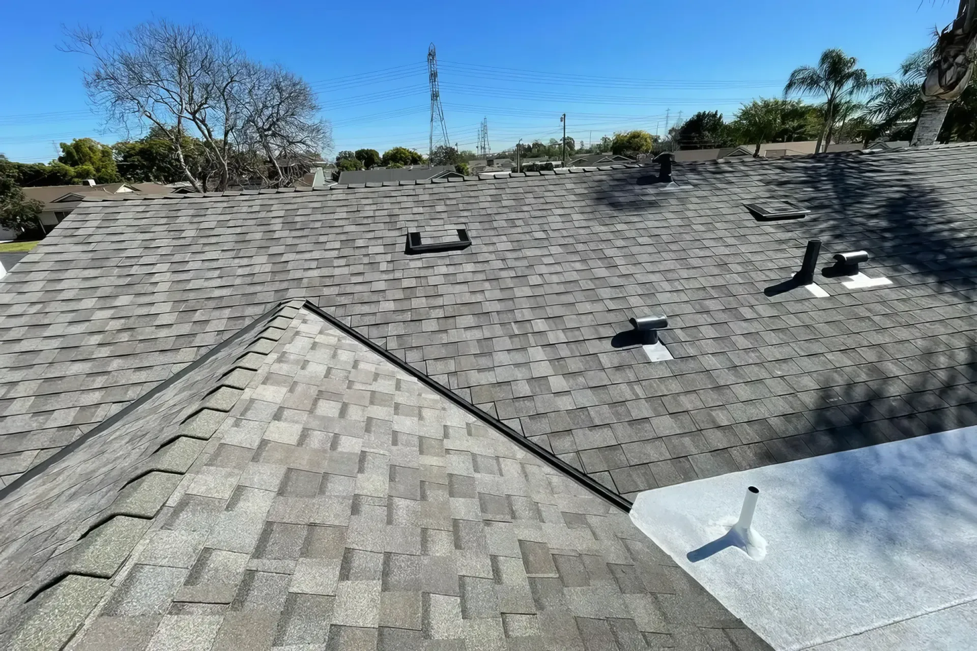 Roof with gray shingles and vent pipes under a clear blue sky