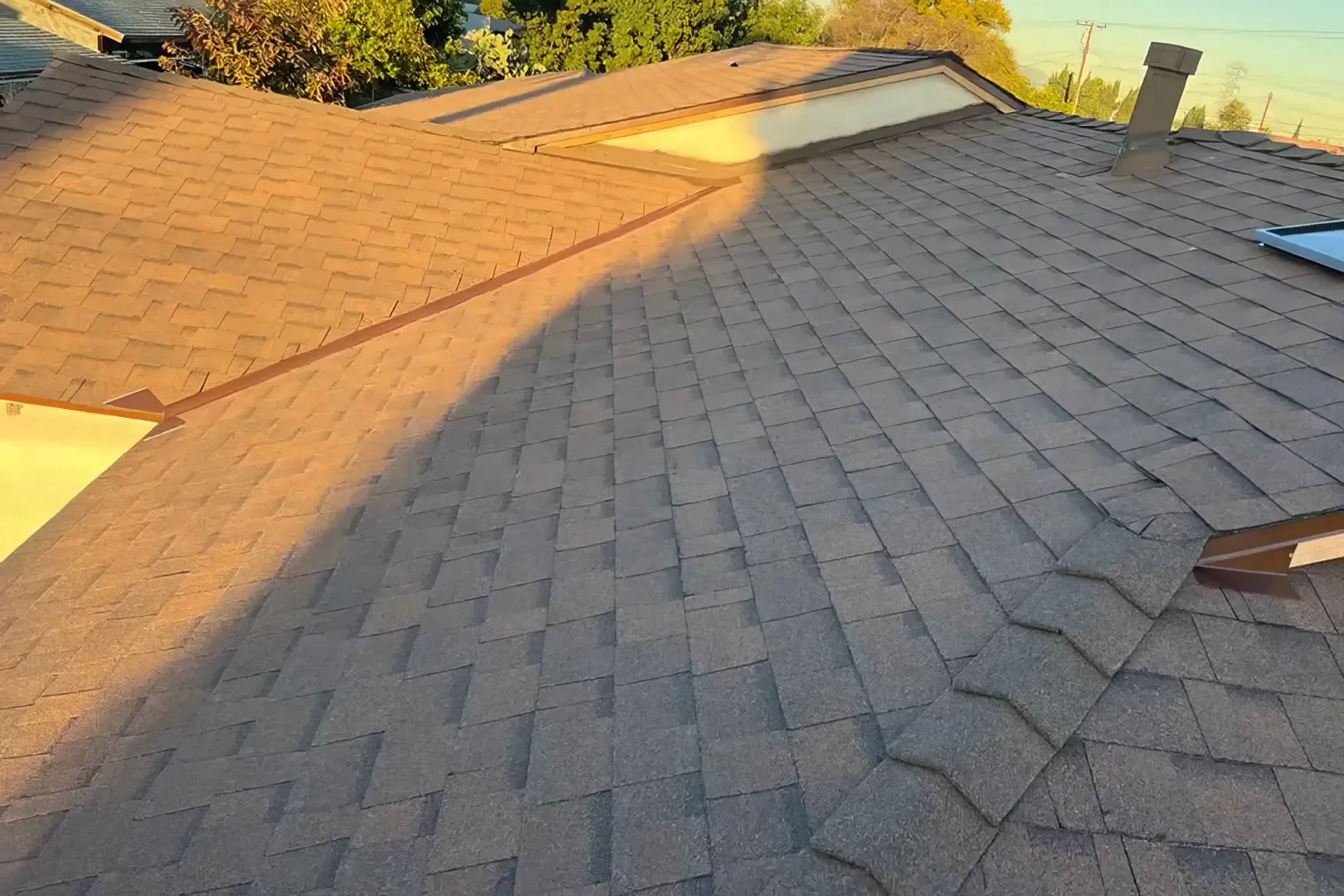 Sunlit shingled roof with a steep slope and chimney, viewed from above