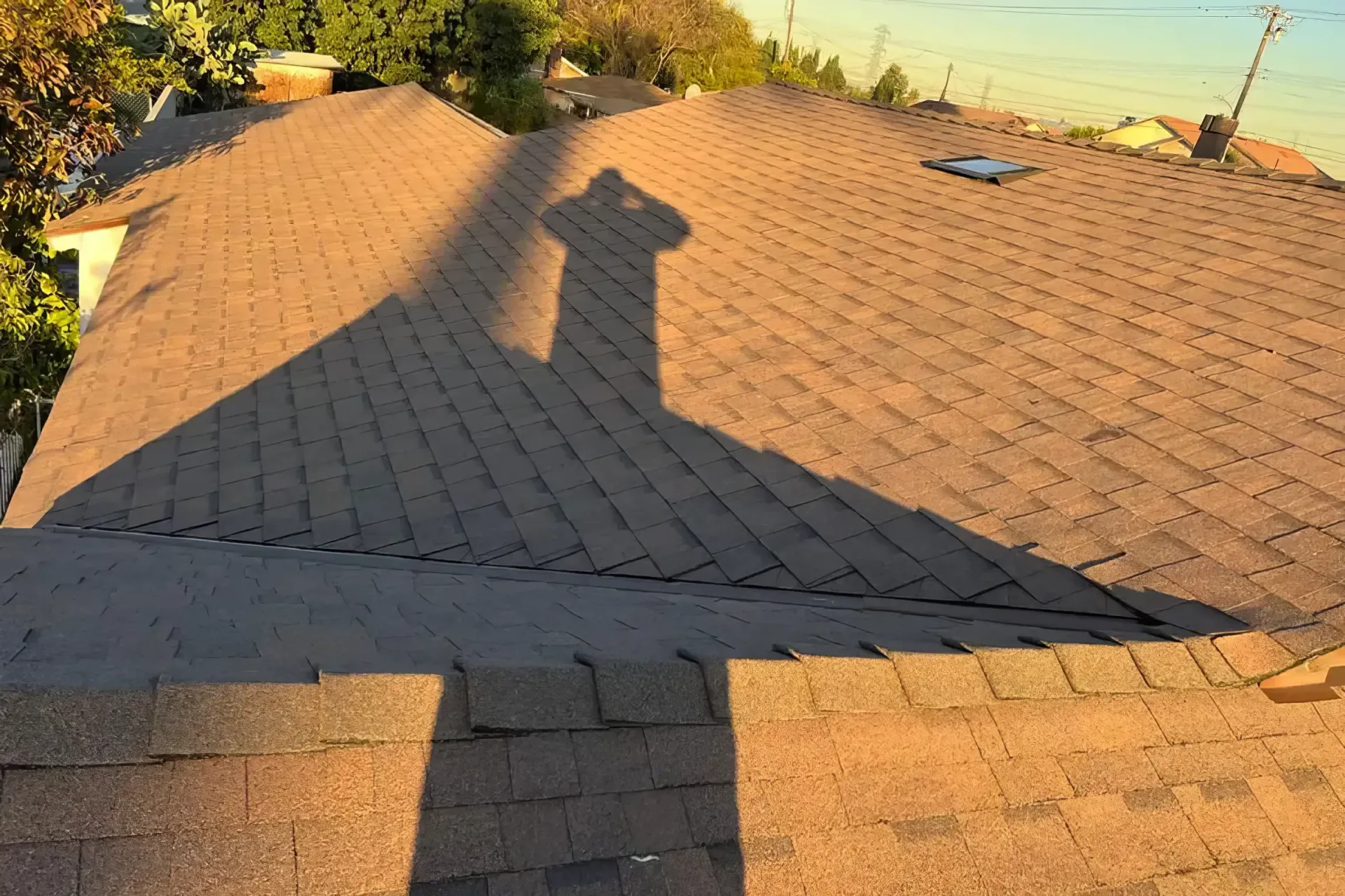 Rooftop with gray shingles at sunset, casting a large shadow across the roof.