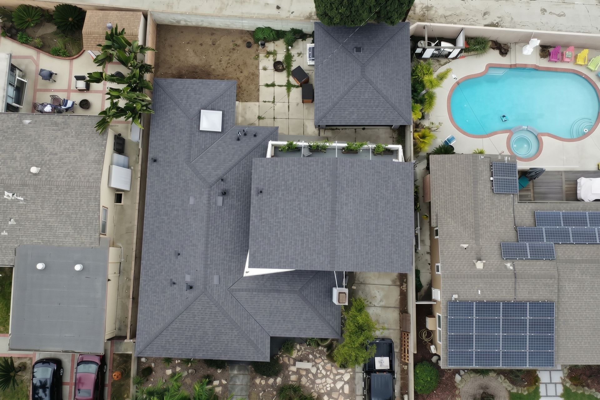 Aerial view of a house with a backyard pool, patio, and solar panels on neighboring roofs.