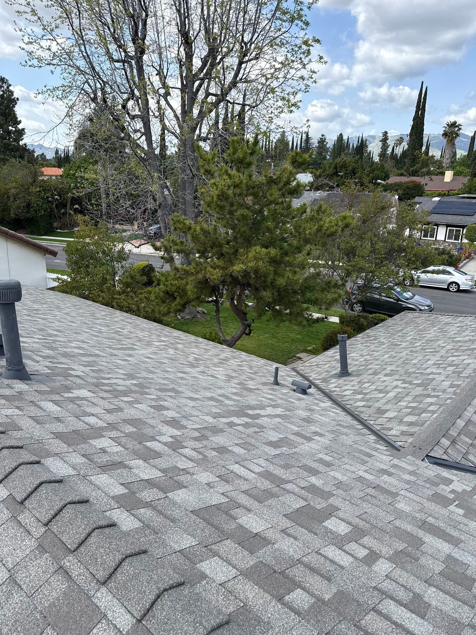 View from a gray shingle roof over trees, houses, and a parking lot under a cloudy sky.