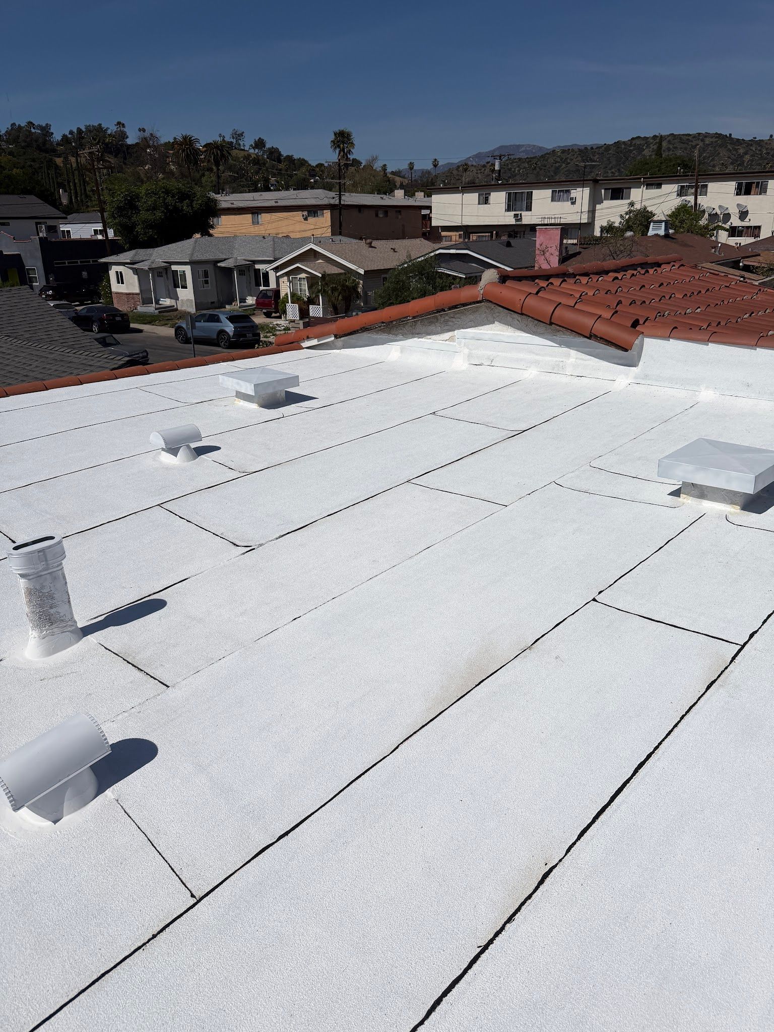 White rooftop with vents overlooking neighboring houses on a sunny day