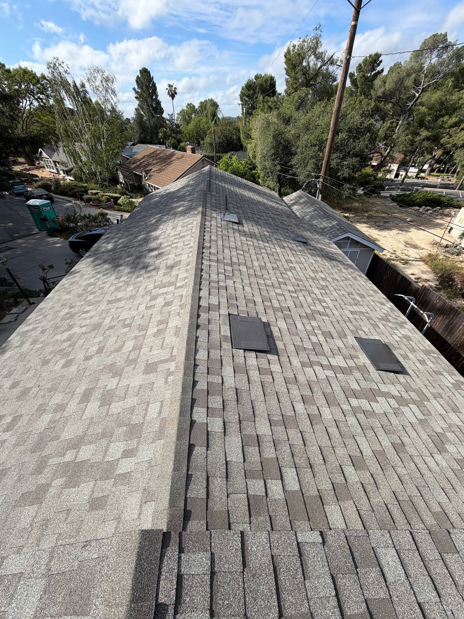 Long, shingled roof on a house under construction, with trees and blue sky in the background