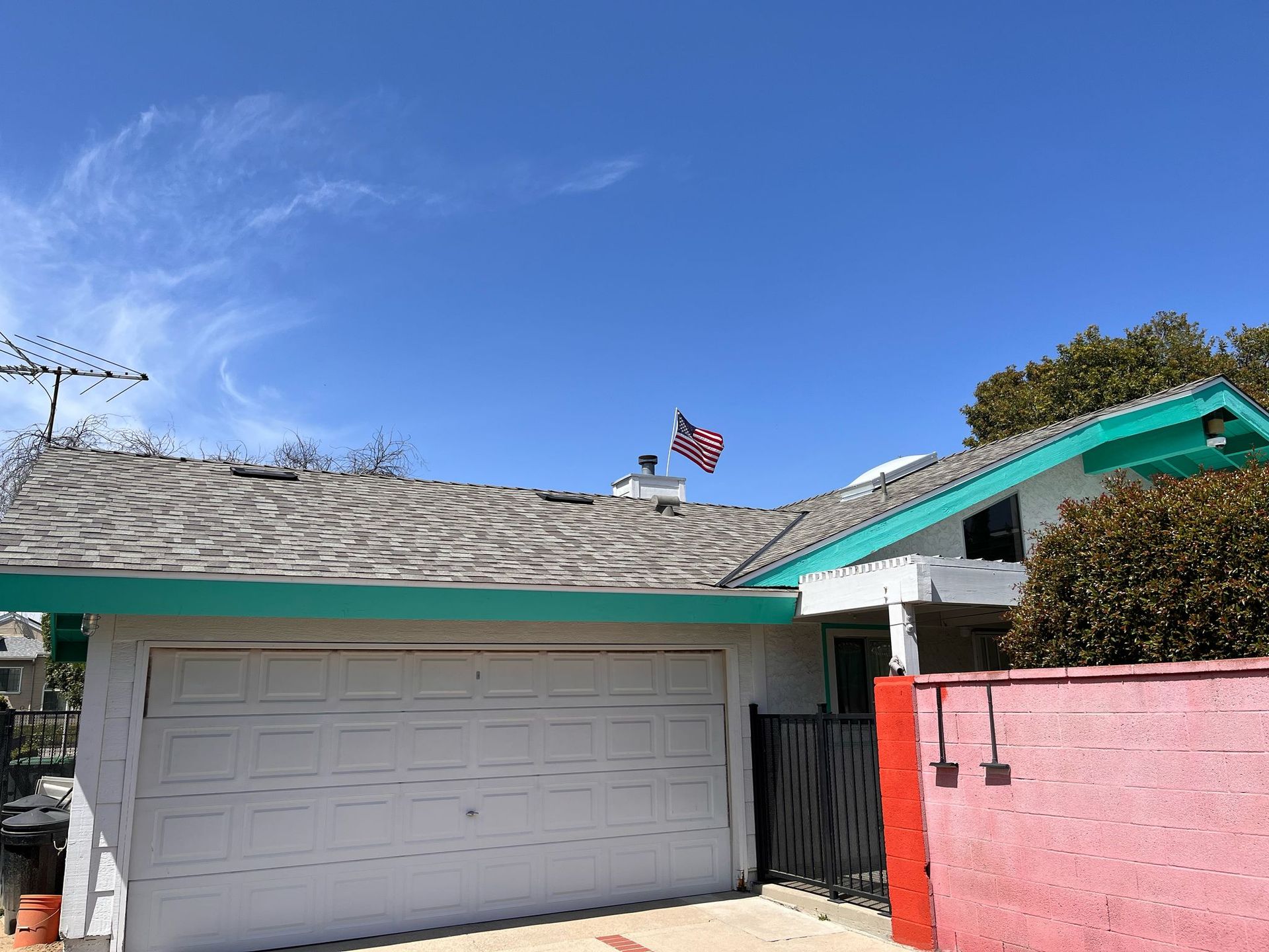 Suburban garage with white door, pink wall, teal roof trim, and American flag against a blue sky