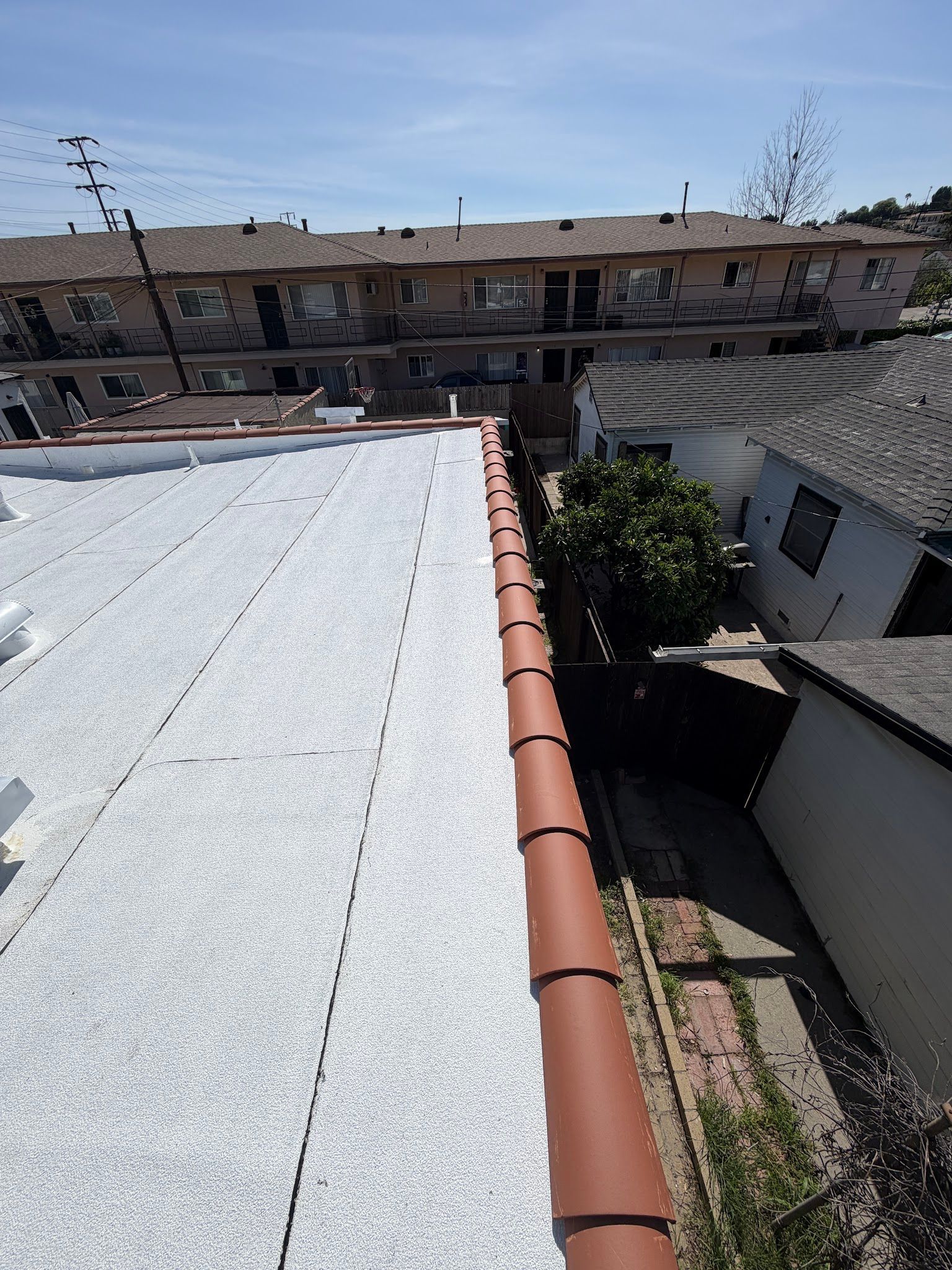 Rooftop view of a white roof, terracotta trim, and a courtyard with apartment buildings under a blue sky