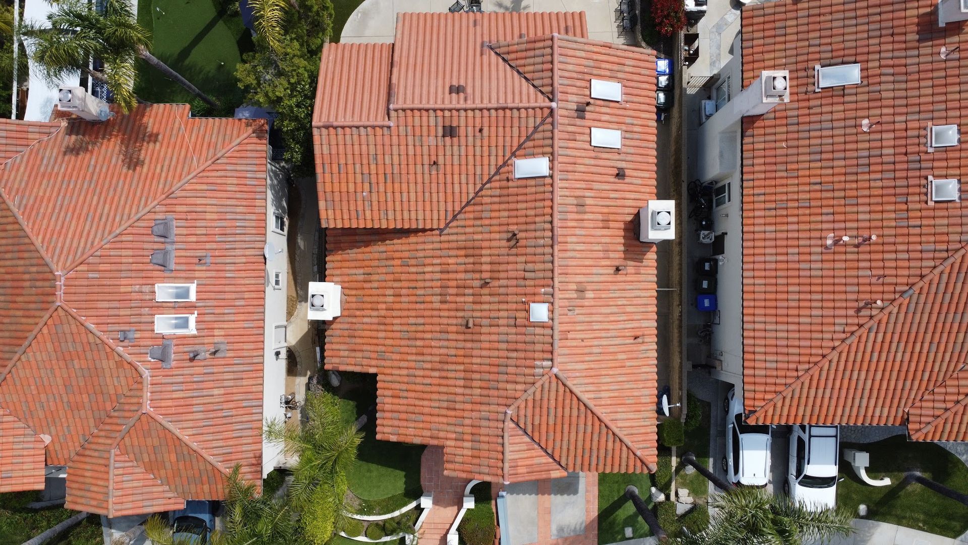 Aerial view of red-tiled rooftops of closely packed houses with trees and parked cars between them