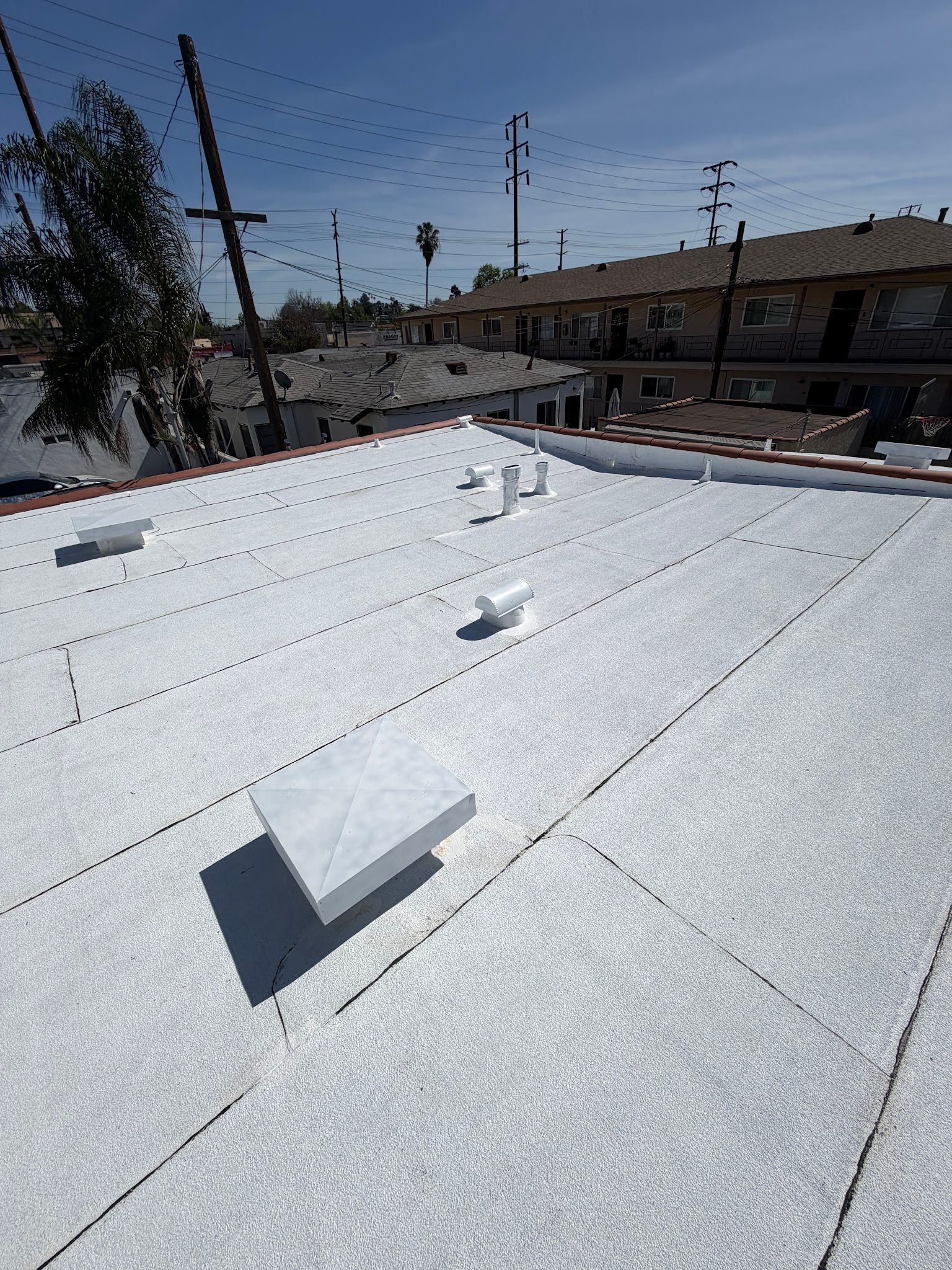 White rooftop with vents under a clear sky, with power lines and buildings in the background.
