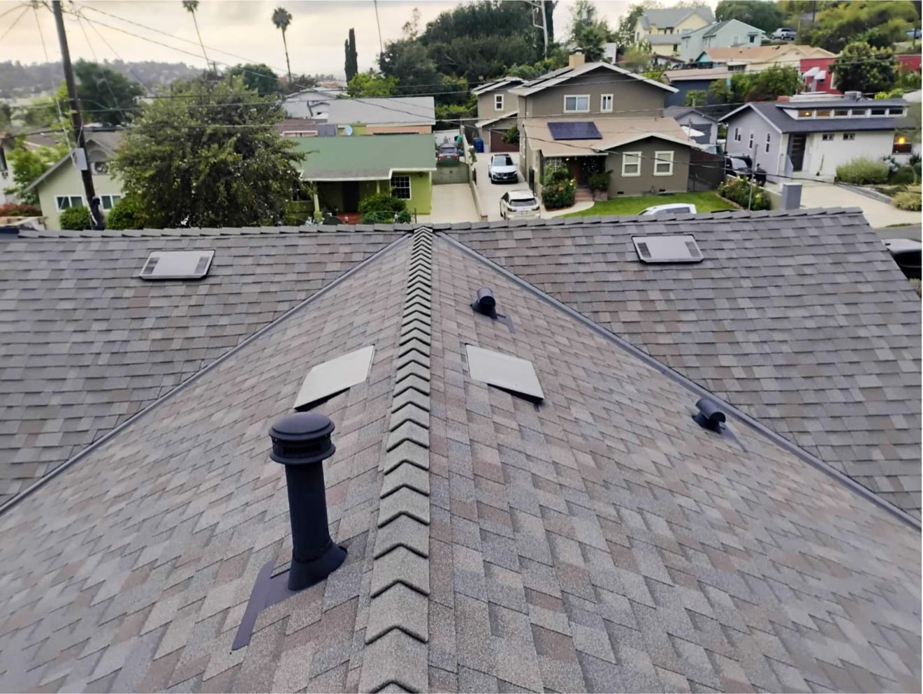 View from rooftop over gray shingle roofs and nearby houses in a residential neighborhood