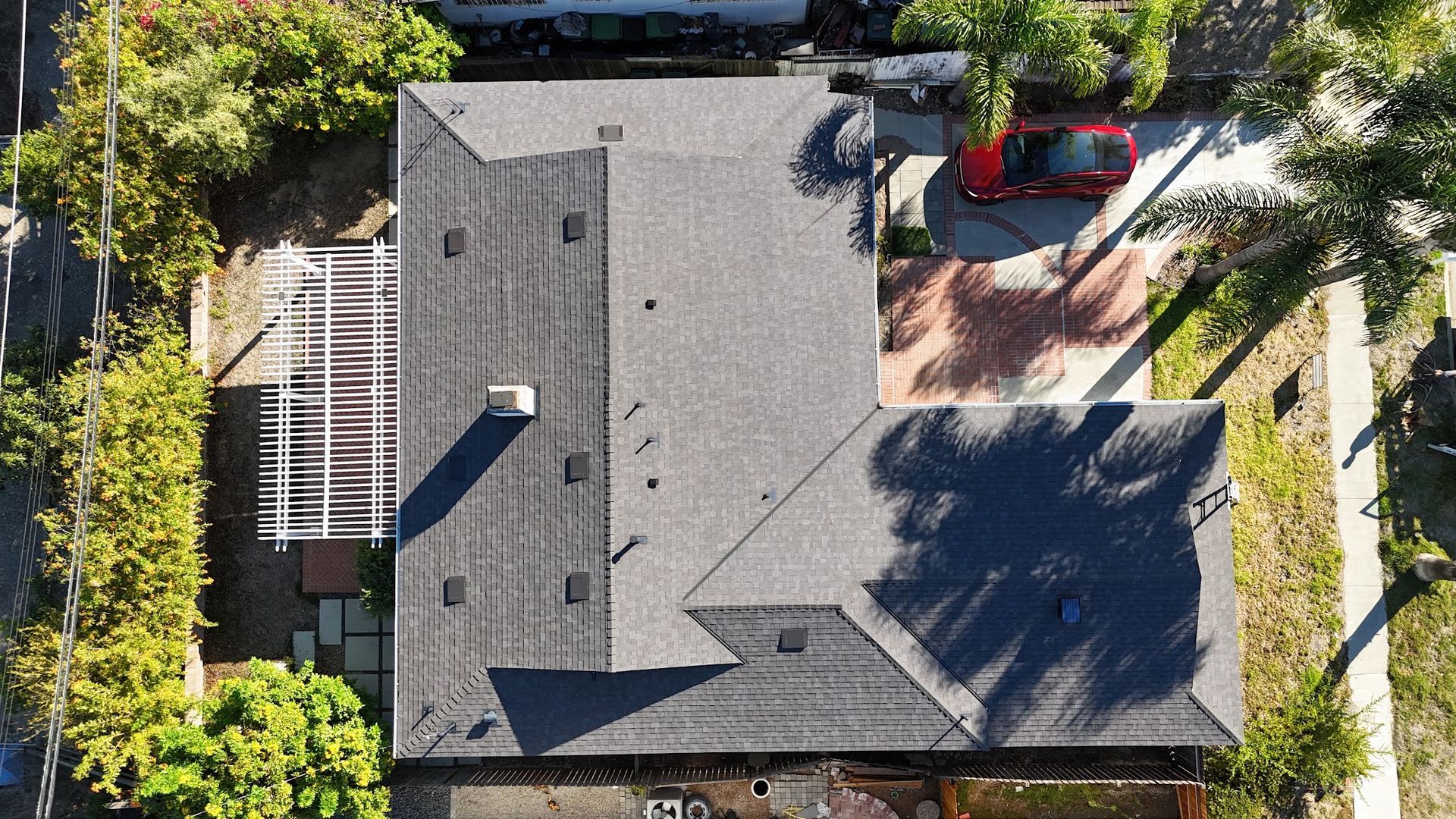 Aerial view of a gray-roofed house with a backyard patio, red seating, and surrounding trees.