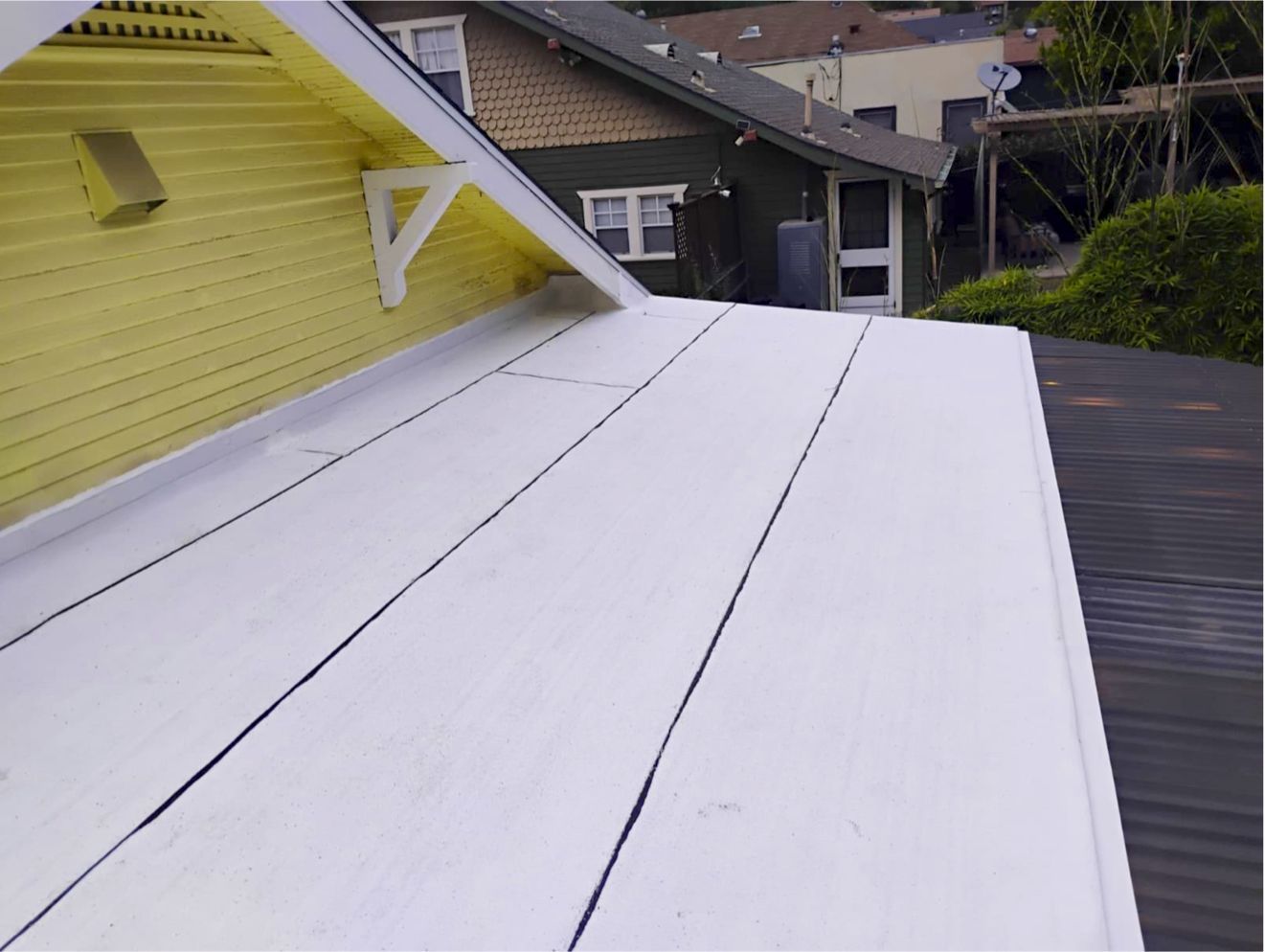 White rooftop or deck beside a yellow house, with neighboring houses in the background.