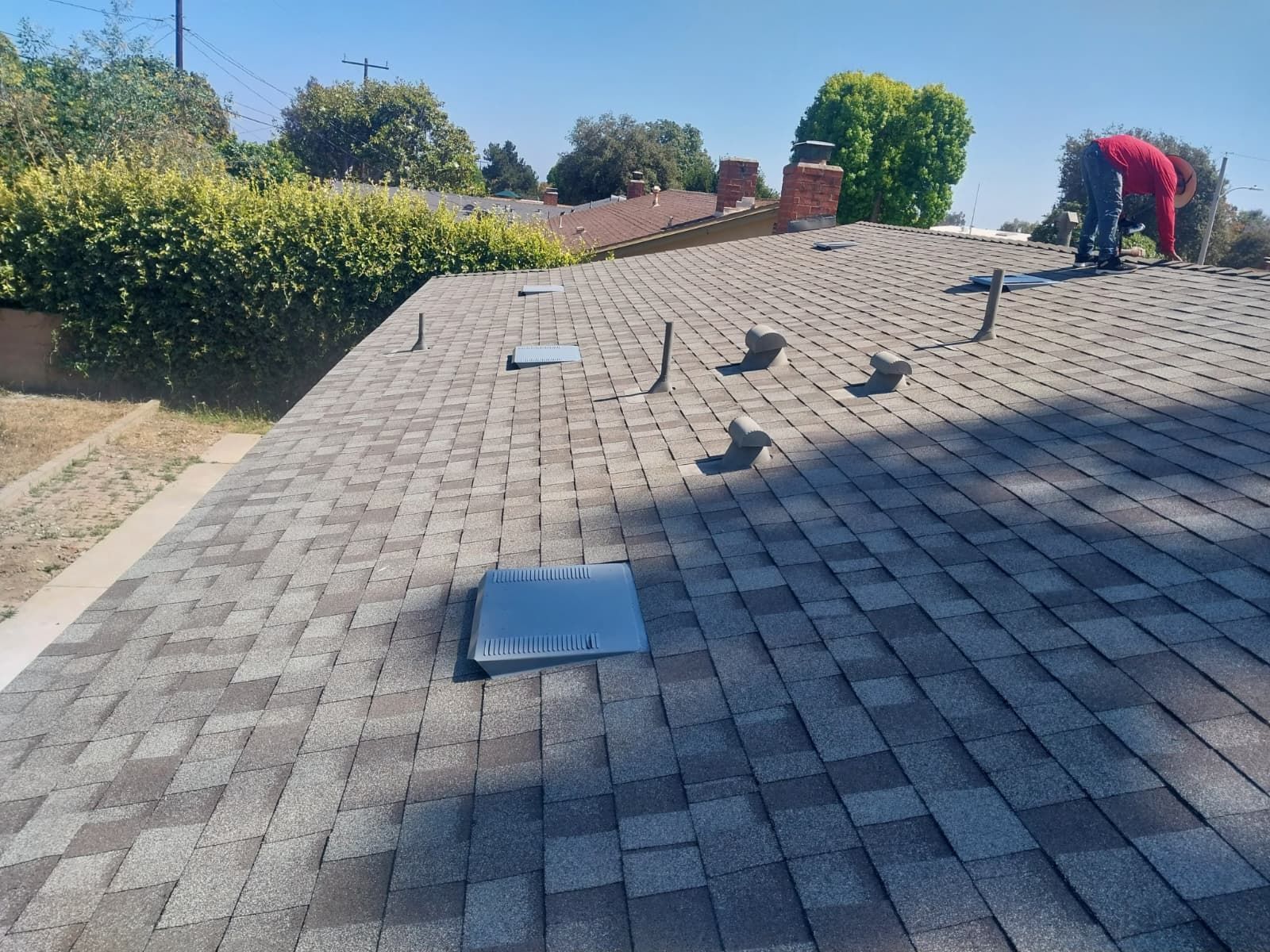 Workers inspecting a shingled roof with vent covers on a sunny day
