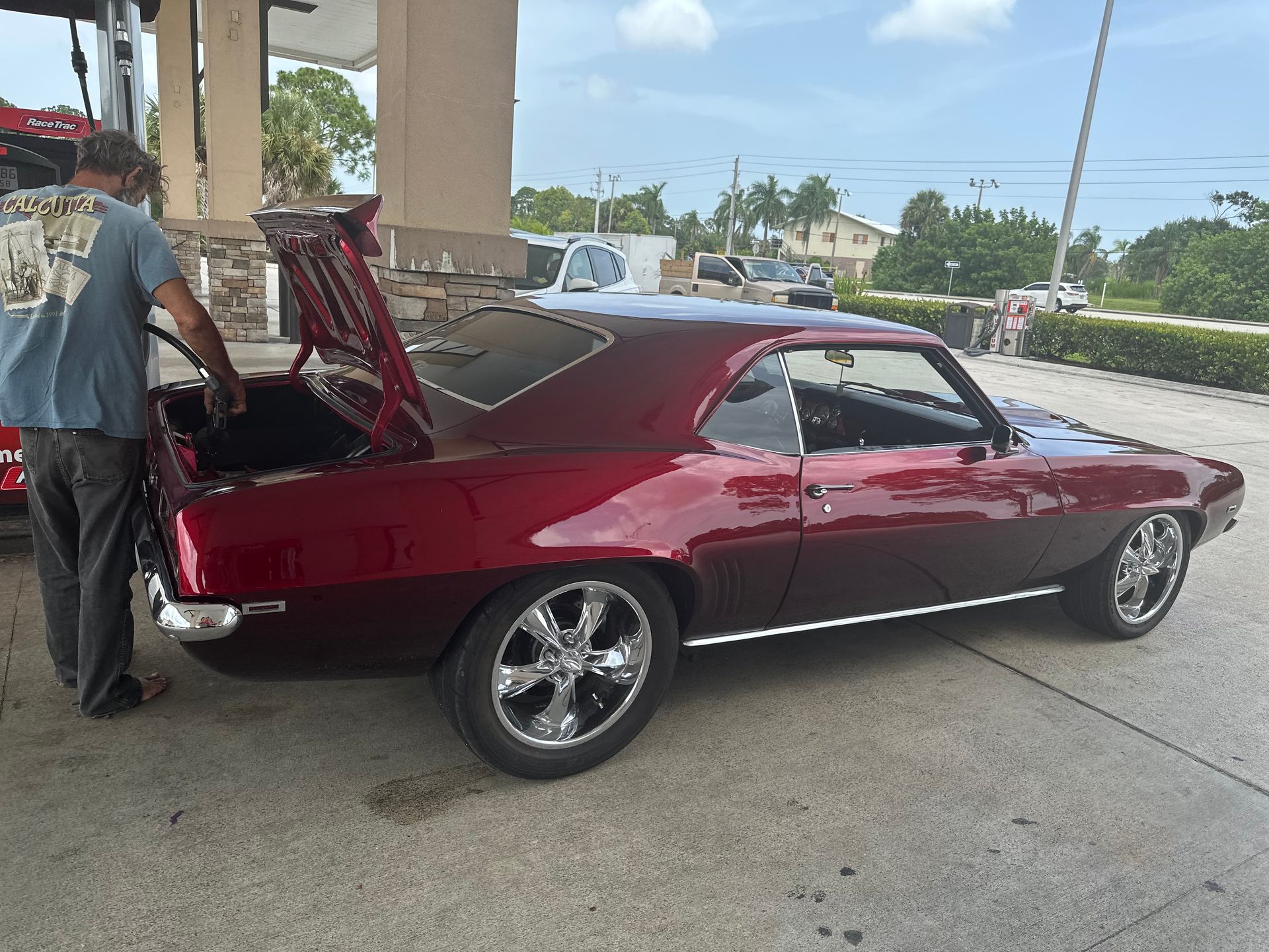 A man is standing next to a red car with the hood up