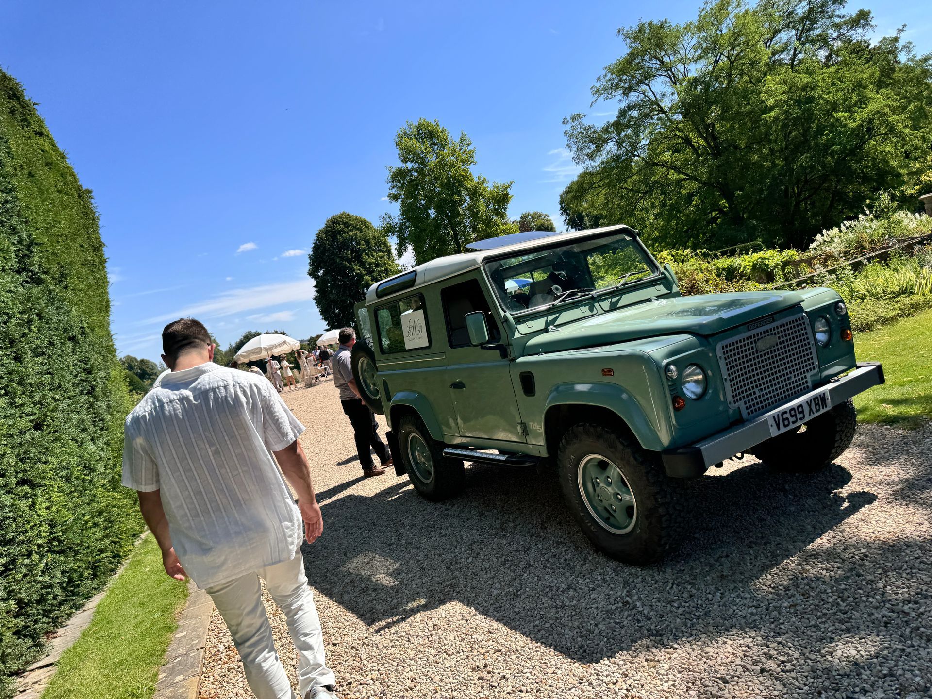 A man is walking towards a green land rover on a gravel road.