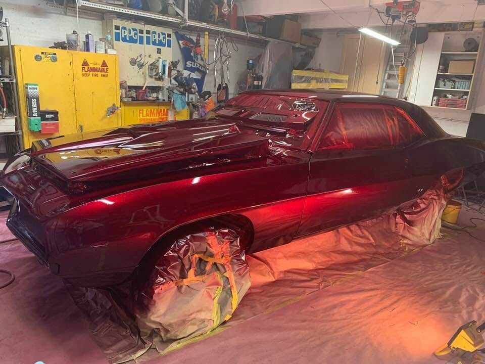 A red car is being painted in a garage.