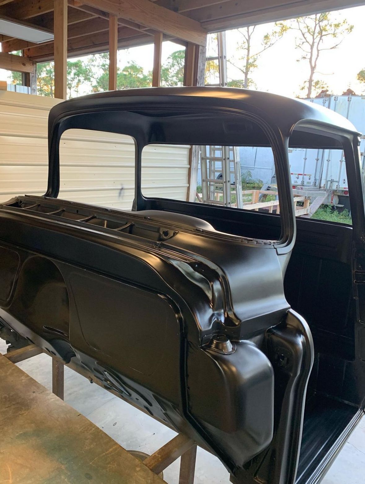 A black truck body is sitting on a wooden table in a garage.