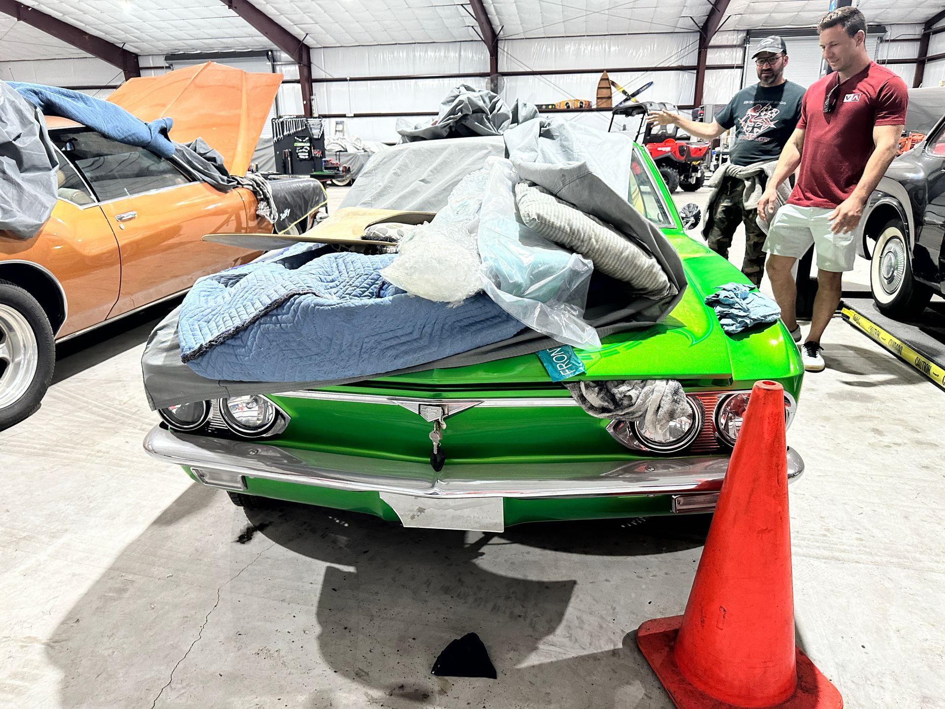 A green car is sitting in a garage next to a red cone.